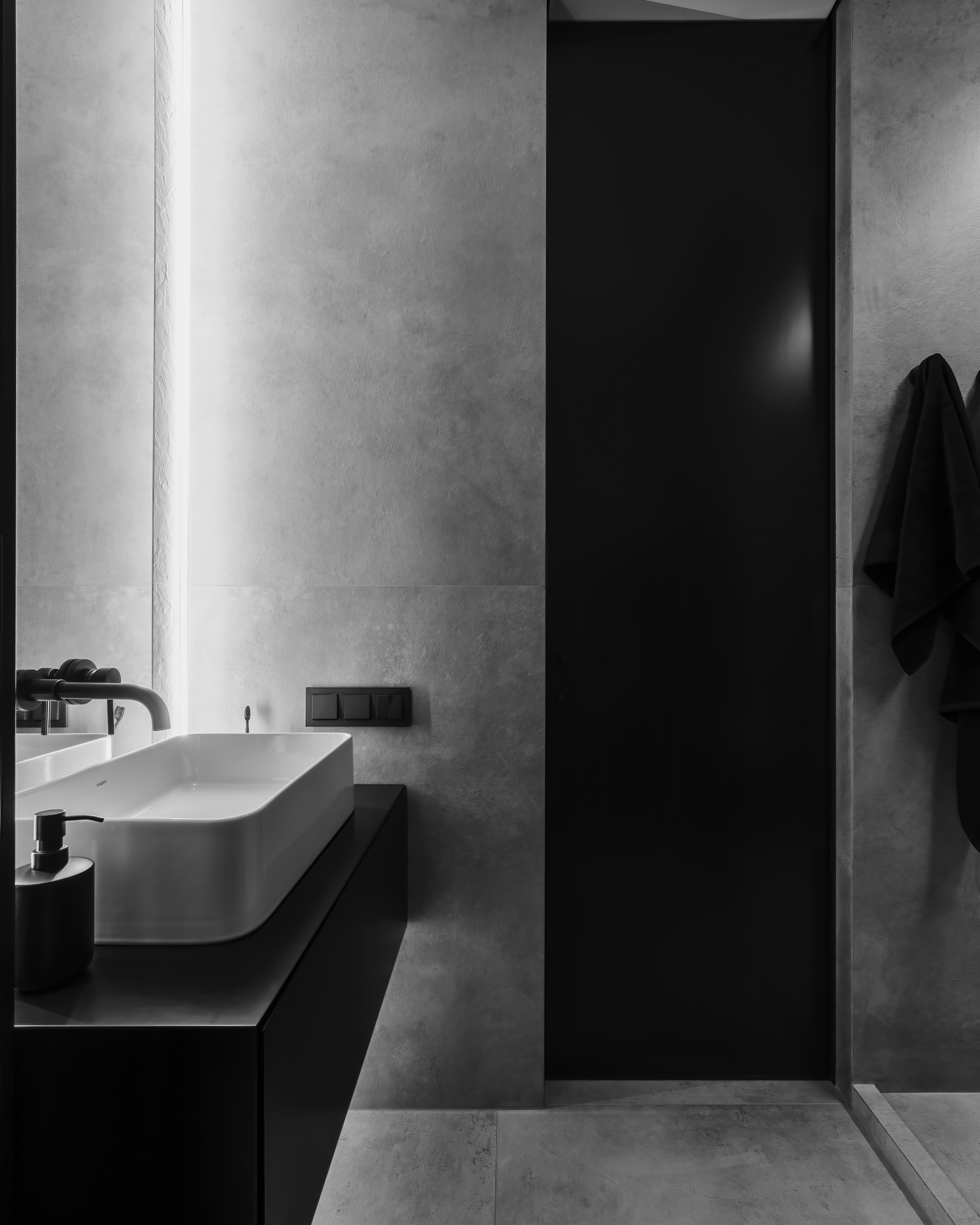 Современная ванная комната в минималистичном стиле с бетонной отделкой стен, подвесной черной тумбой и белой раковиной, встроенной подсветкой и черными акцентами. Автор дизайна Анатолий Котов, интерьер снят фотографом Сергеем Денисенко.