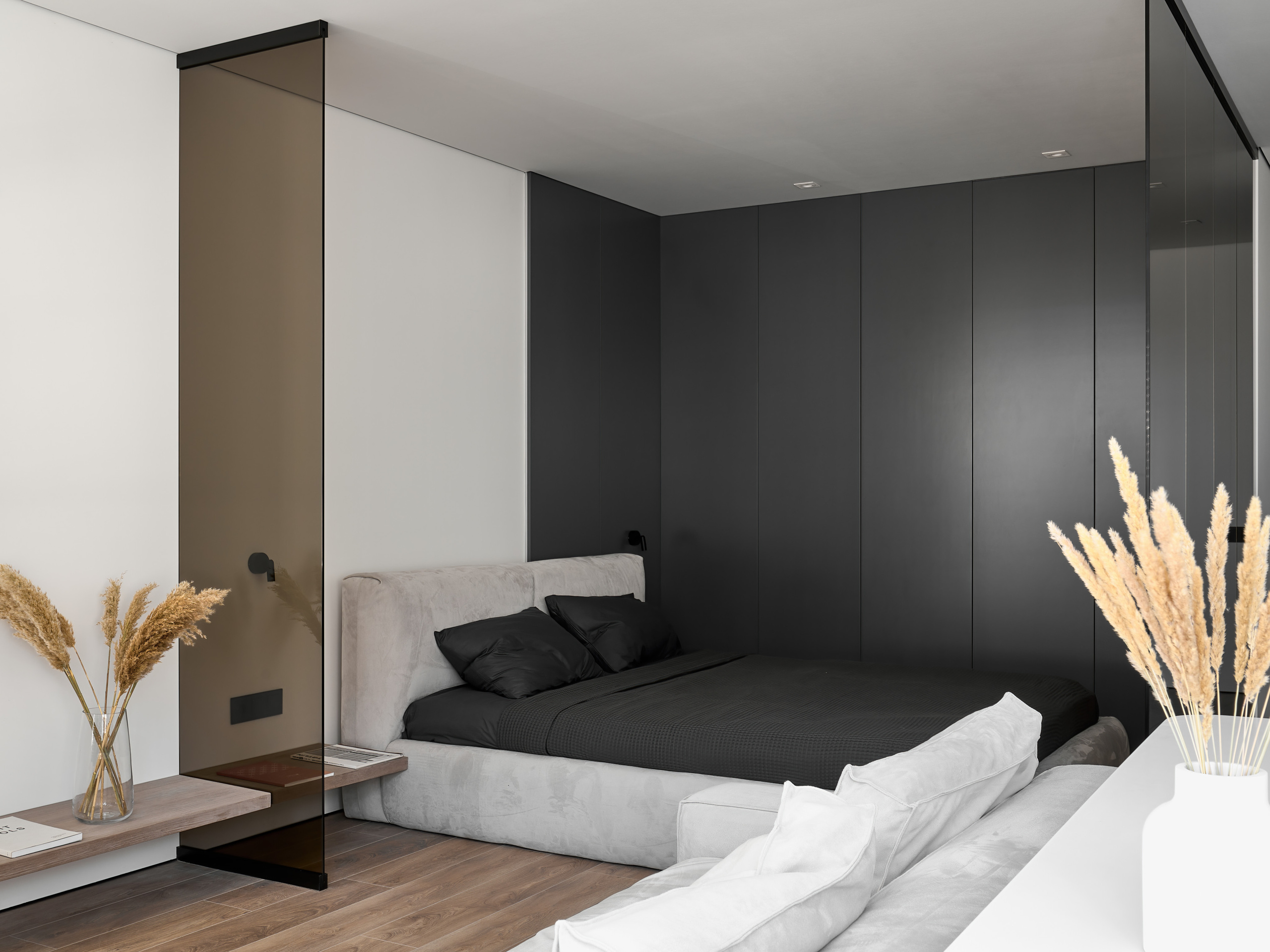 Современная спальня в минималистичном стиле с темными панелями, мягким серым изголовьем и черным текстилем на кровати, дизайнер Анатолий Котов, фотограф Сергей Денисенко, интерьер с акцентом на геометрию и чистые линии.