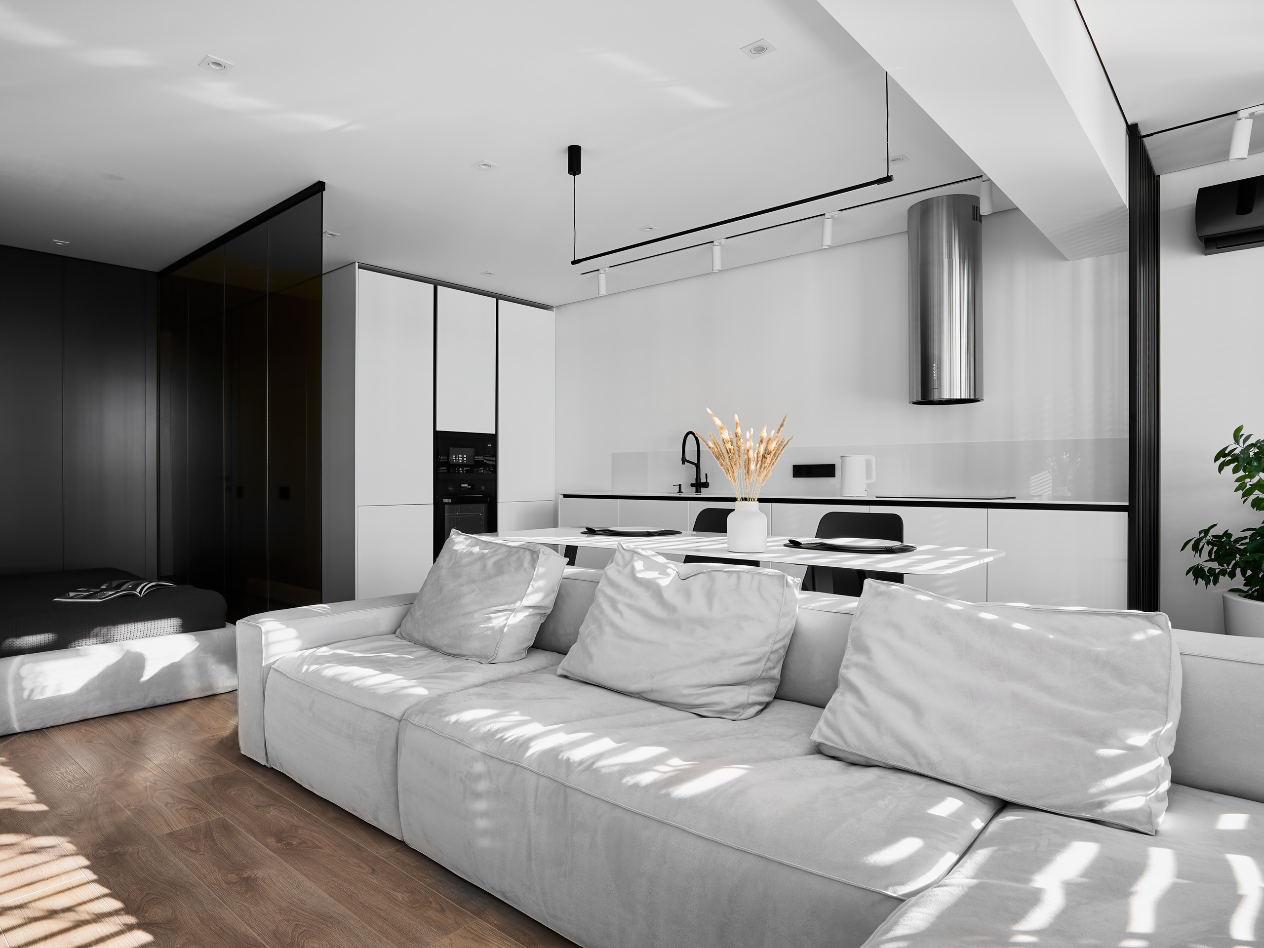 Просторная студия с кухней и гостиной в едином современном стиле, белый диван с мягкими подушками, деревянный пол, минималистичная кухня и обеденный стол с декором. Атмосферный дизайн Анатолия Котова, фотография Сергея Денисенко.