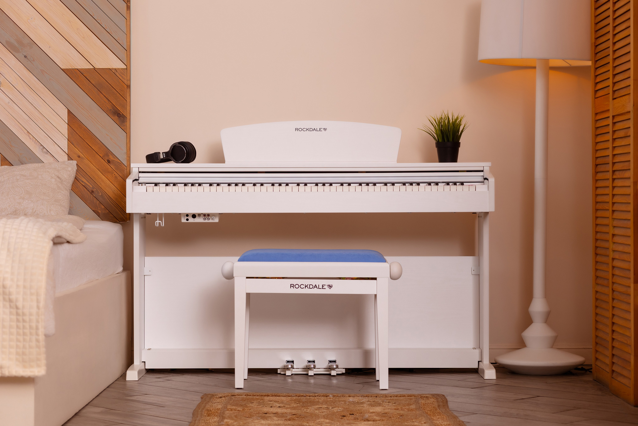 У стены стоит белое  пианино, перед ним белый табурет