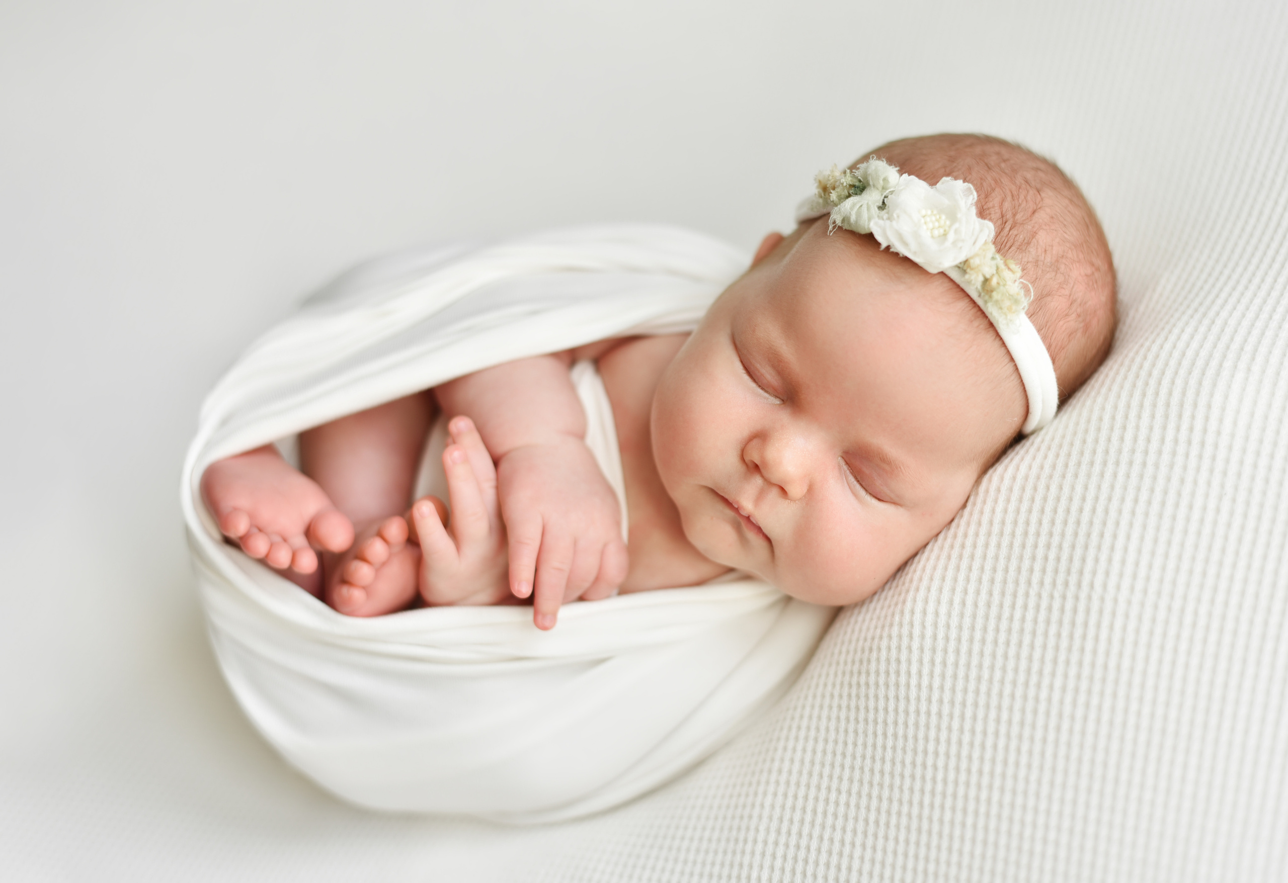 Новорожденная девочка в белой одежде на белом фоне.