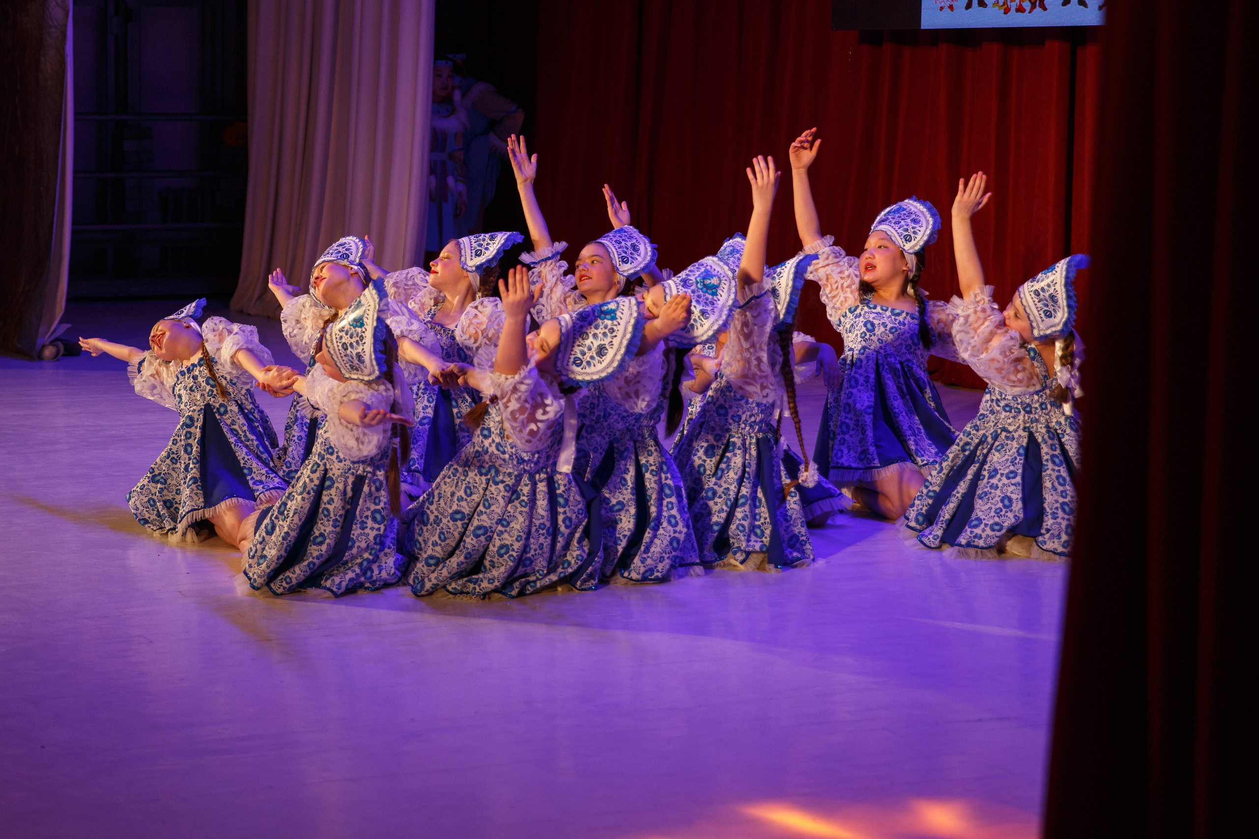 Группа детей танцует на сцене в нарядных костюмах.