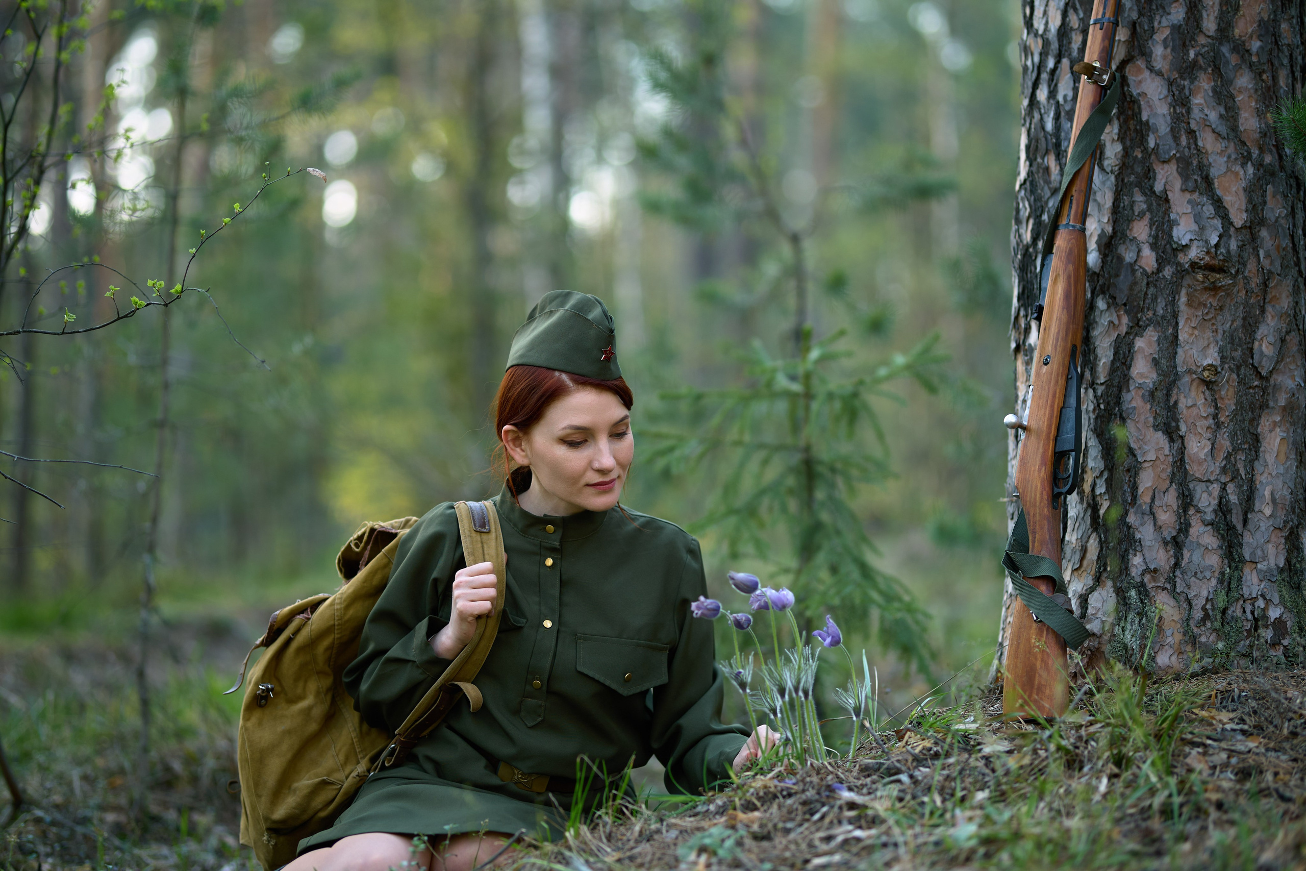 тематическая фотосессия на военную тему, девушка сидит с винтовкой в лесу около цветов