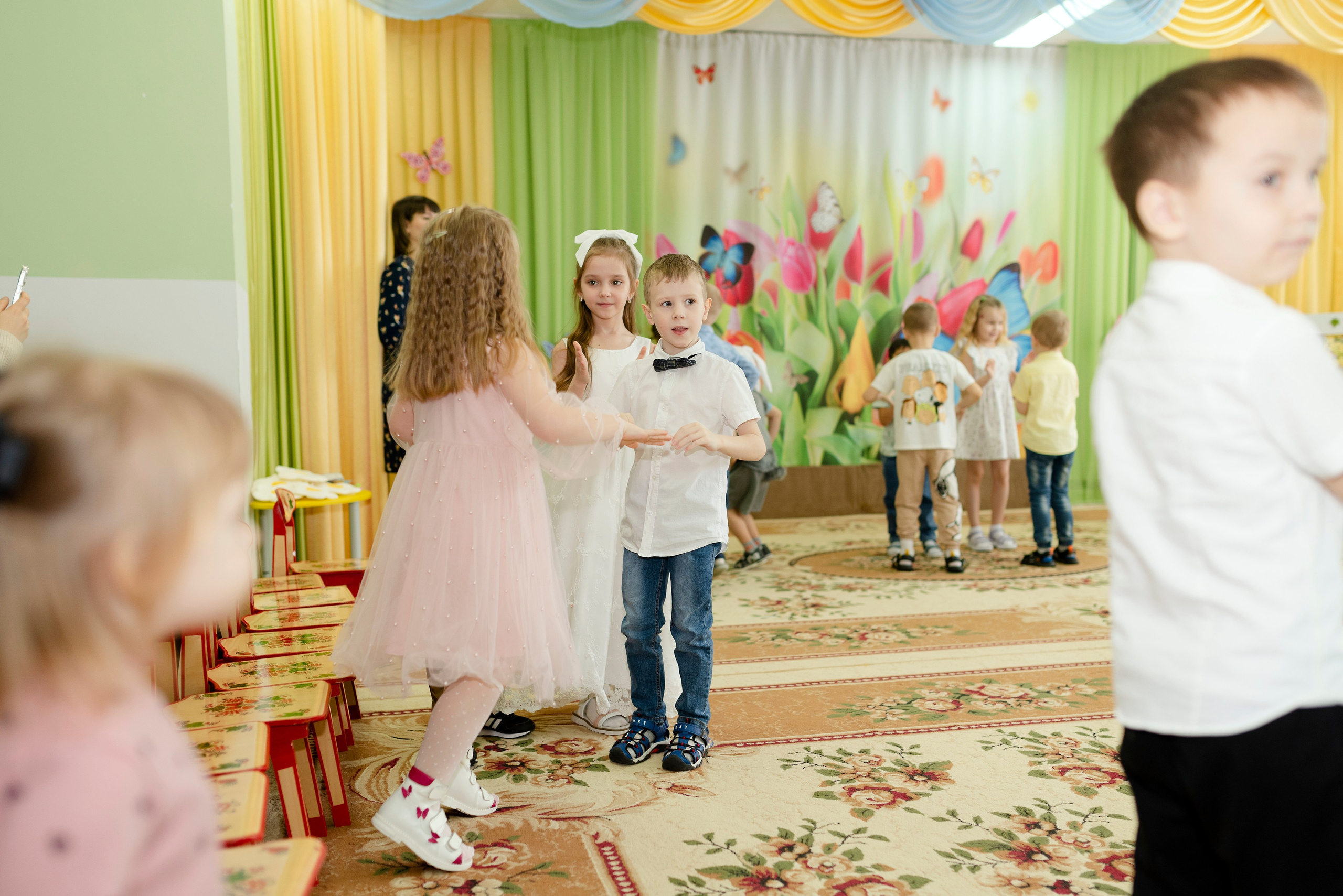 Дети танцуют веселый танец в праздничных костюмах на утреннике 8 марта в детском саду.