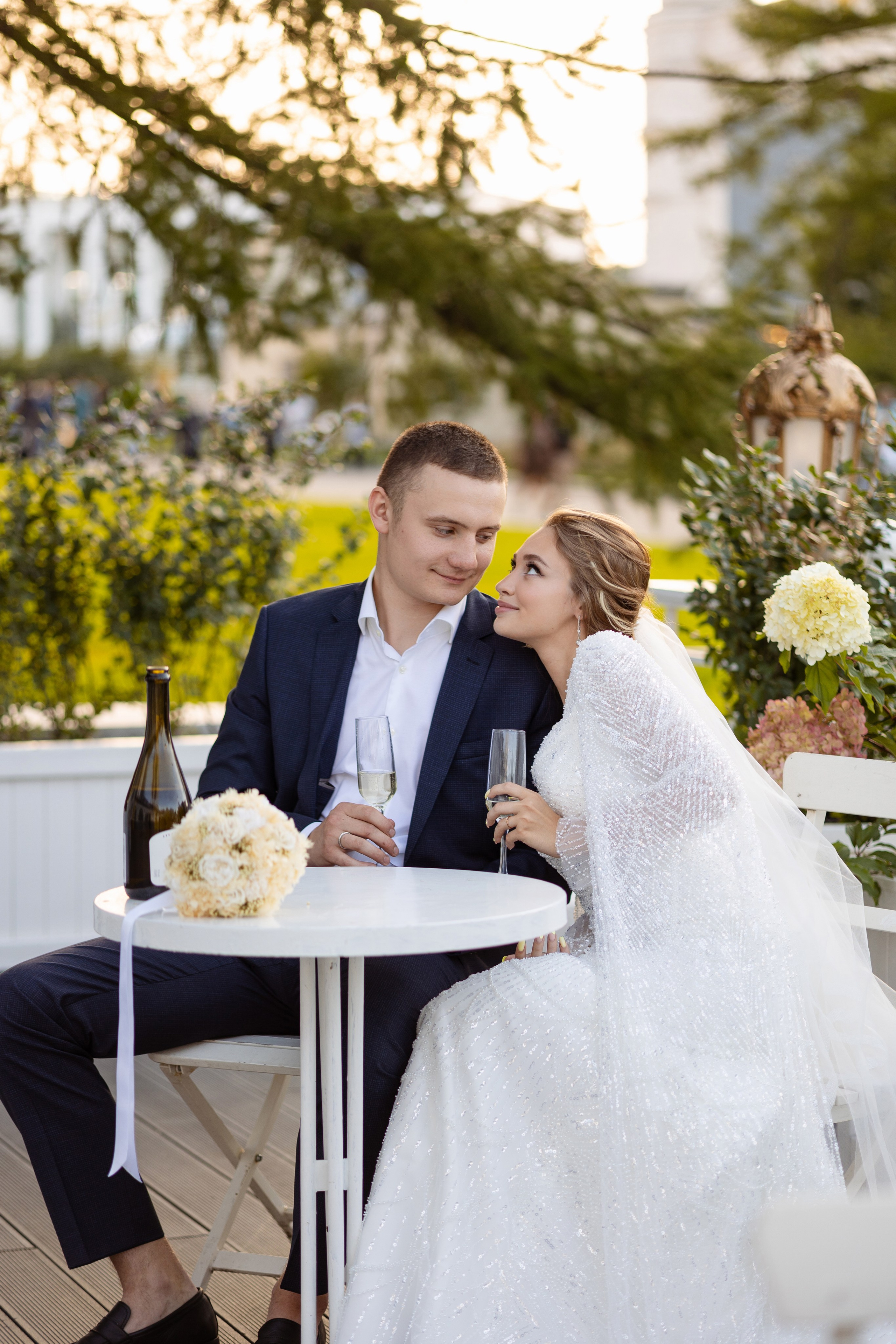 Молодые сидят за круглым столом, на котором лежит букет невесты.