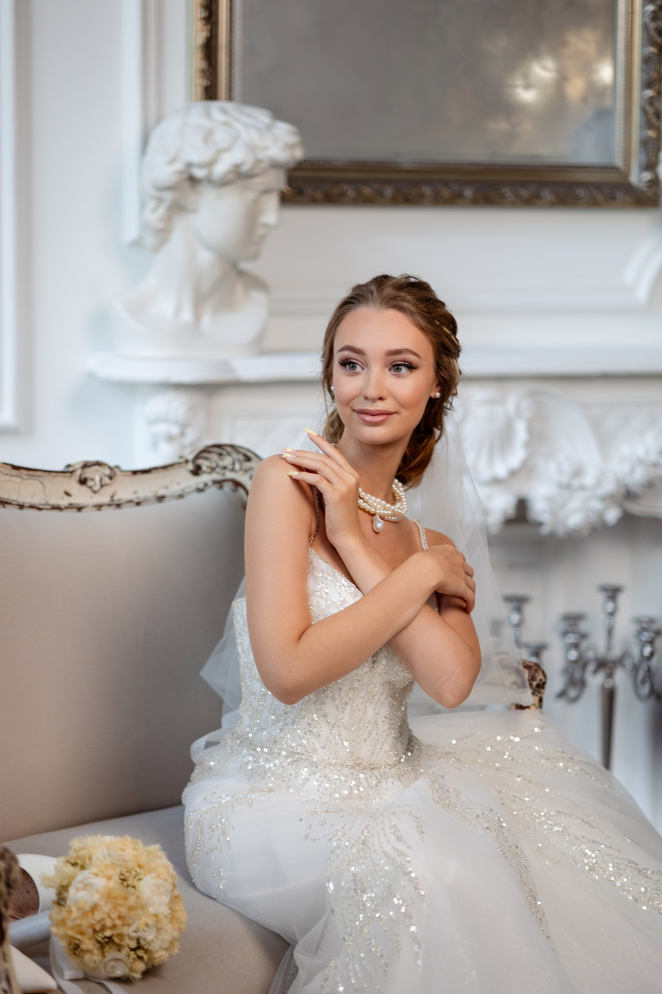 Невеста сидит на диване, обнимая себя руками.