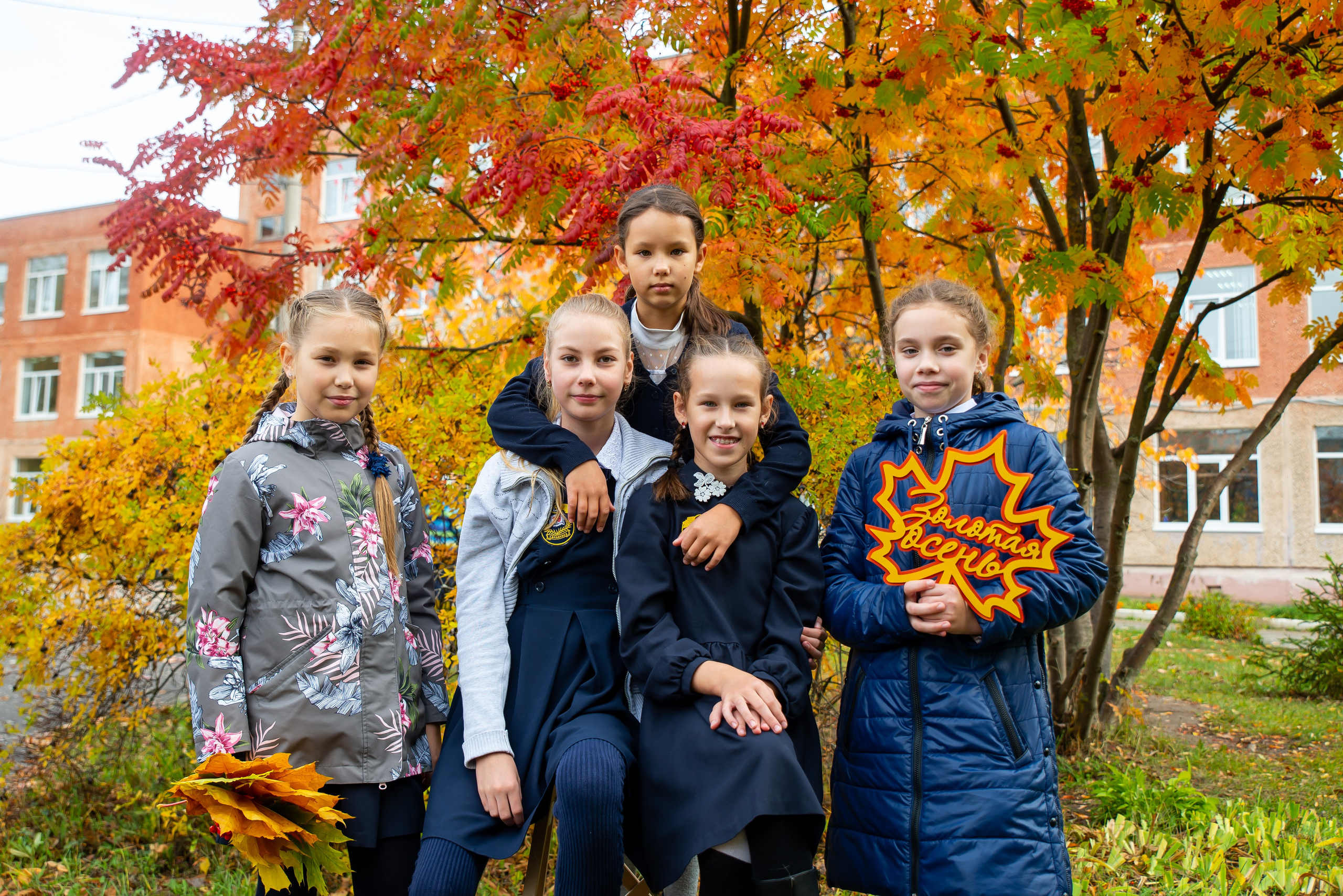 Школьницы на фоне осенней рябины, усыпанной красными гроздьями ягод.