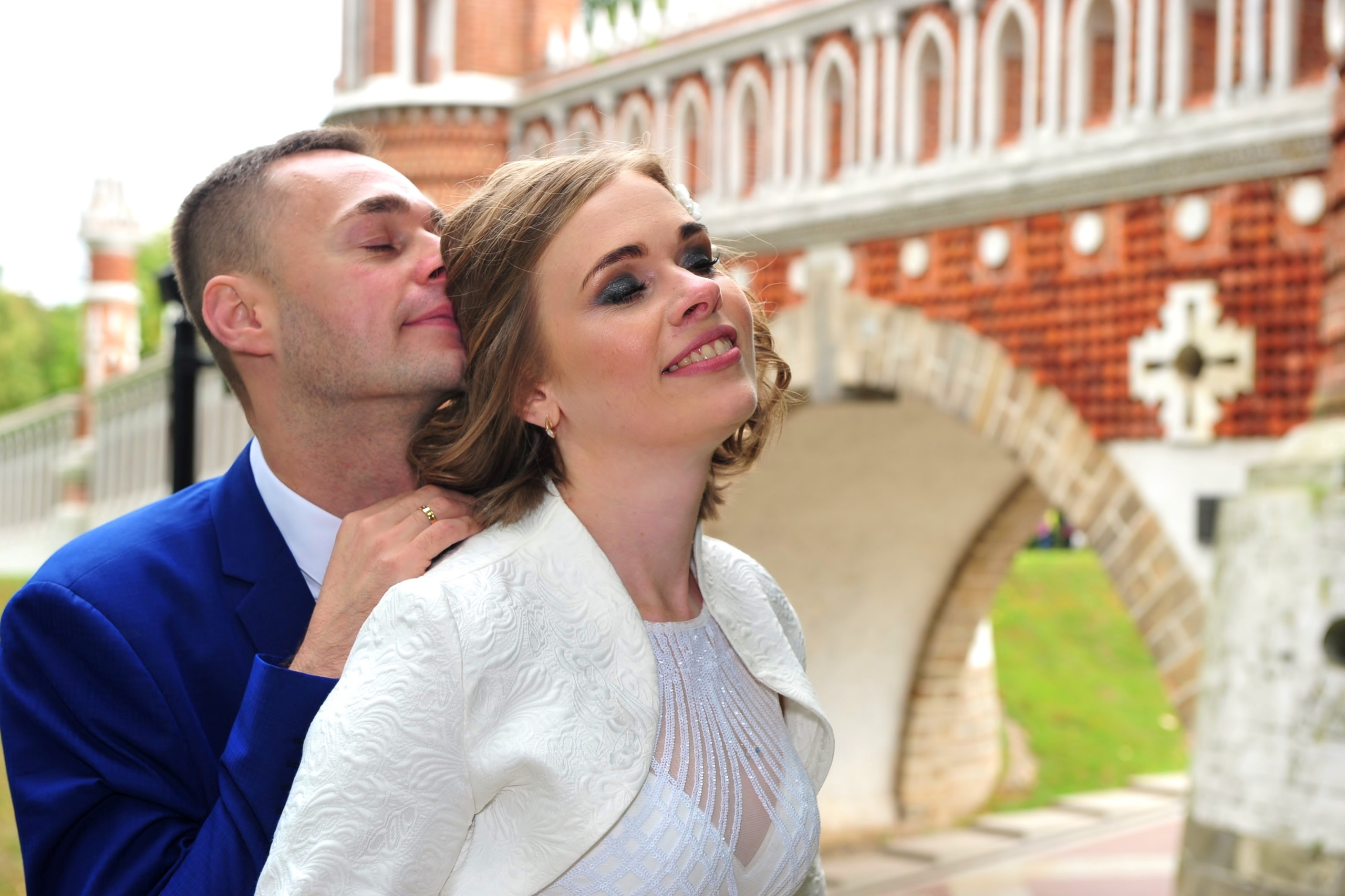 Свадьба в Царицыно хмурым прохладным летним днём, новобрачные обнимаются на фоне арки моста из красного кирпича и белого камня