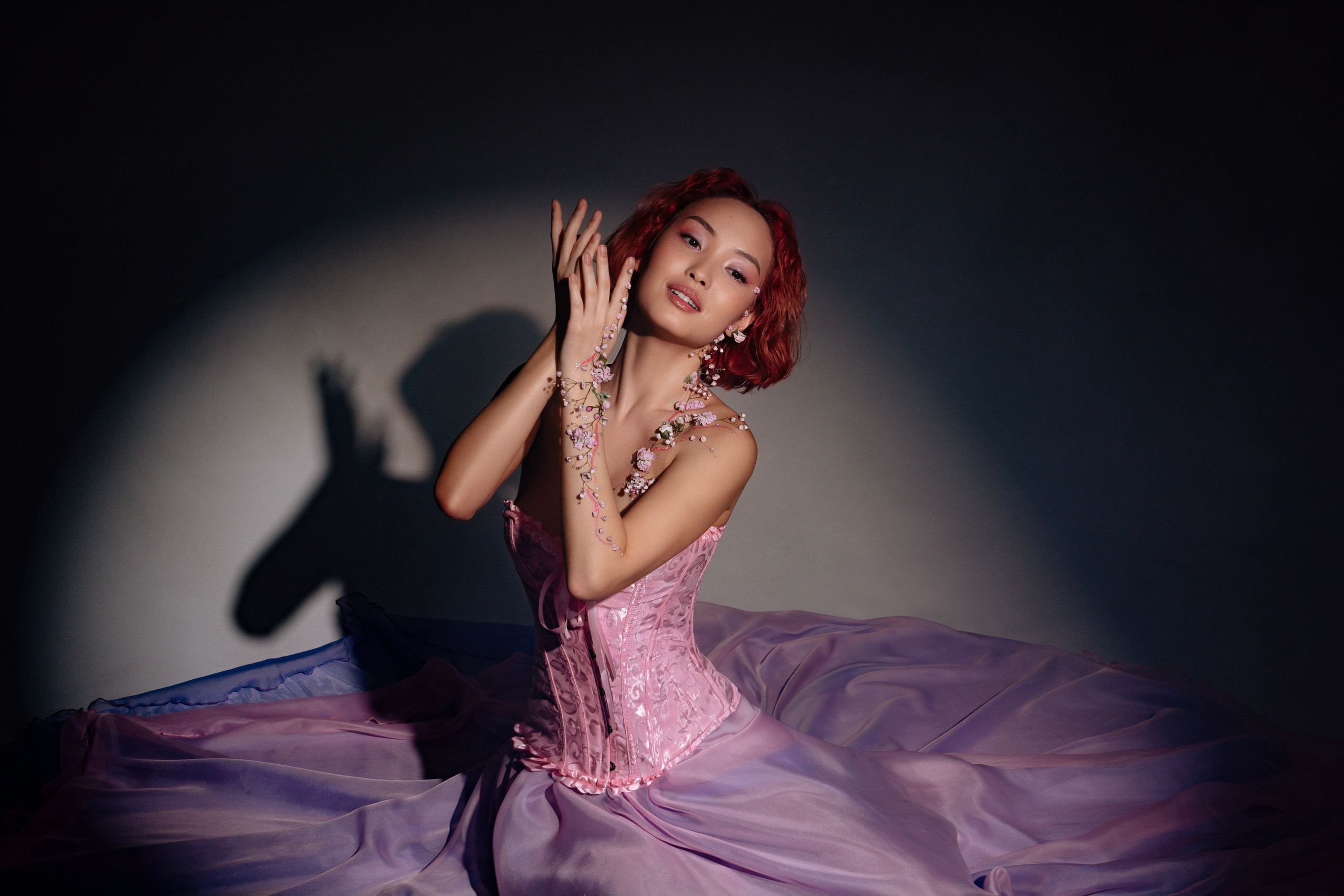 Стройная девушка в струящемся розовом платье, декорированном живыми цветами, олицетворяет пробуждение природы после зимней спячки, излучая свежесть и нежность весеннего сезона.