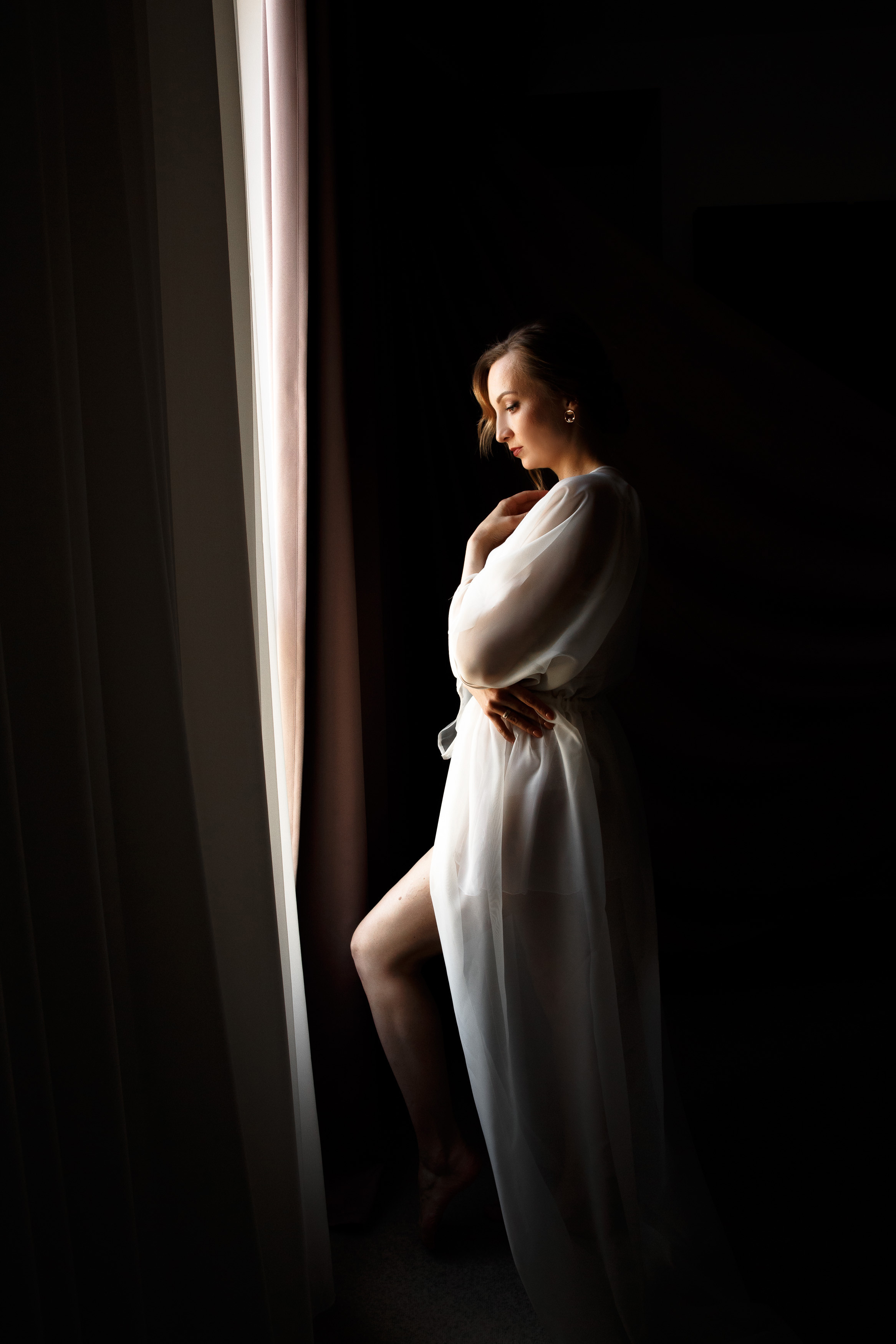 невеста в пеньюаре смотрит в окно в номере отеля люкс