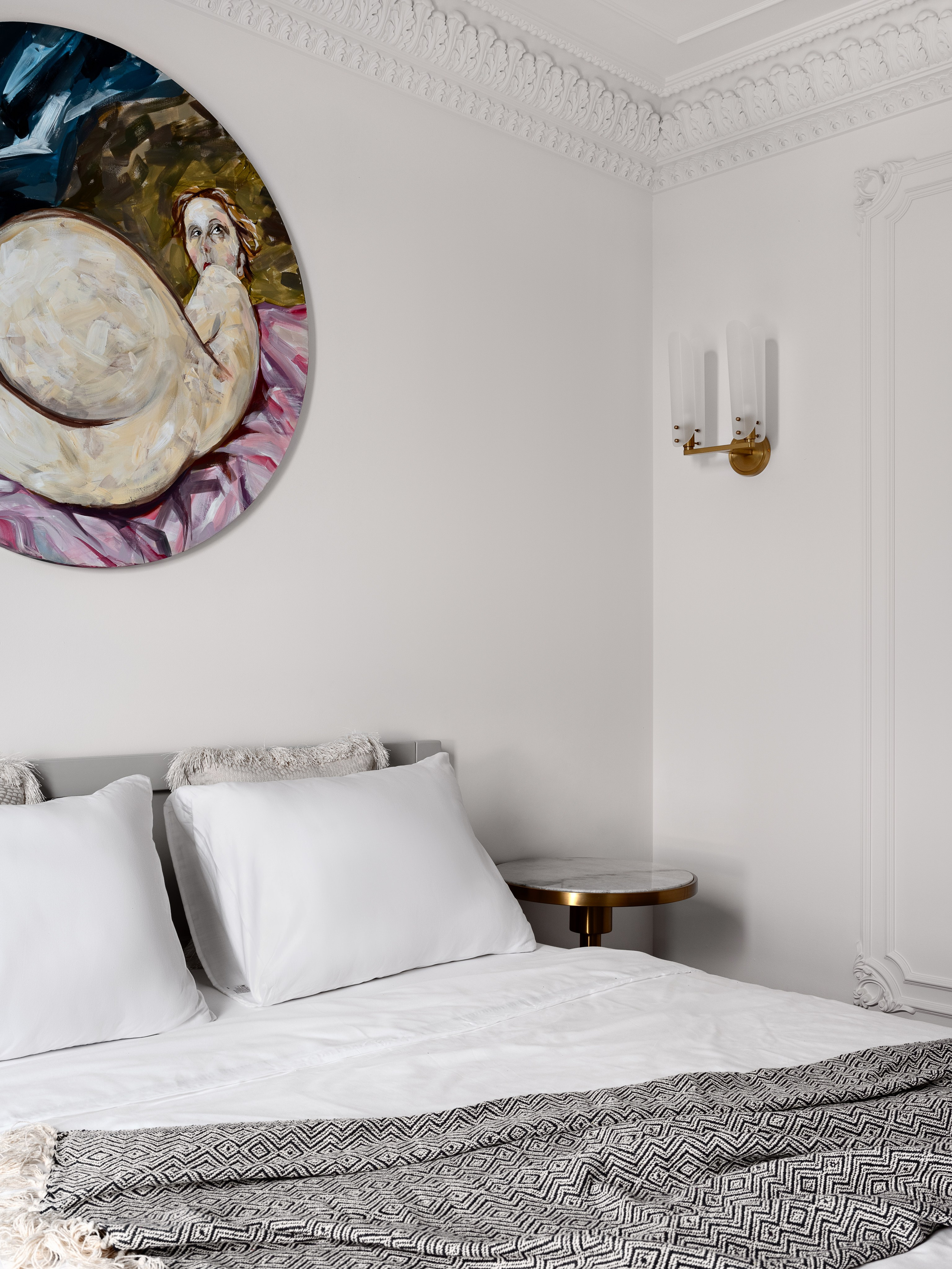 Белая спальня с изысканным лепным декором на потолке, круглой картиной над изголовьем, минималистичной мебелью и золотистым бра. Дизайнер Антон Логинов, стилист Алёна Мощенская, фотограф Сергей Денисенко создали гармоничный современный интерьер.