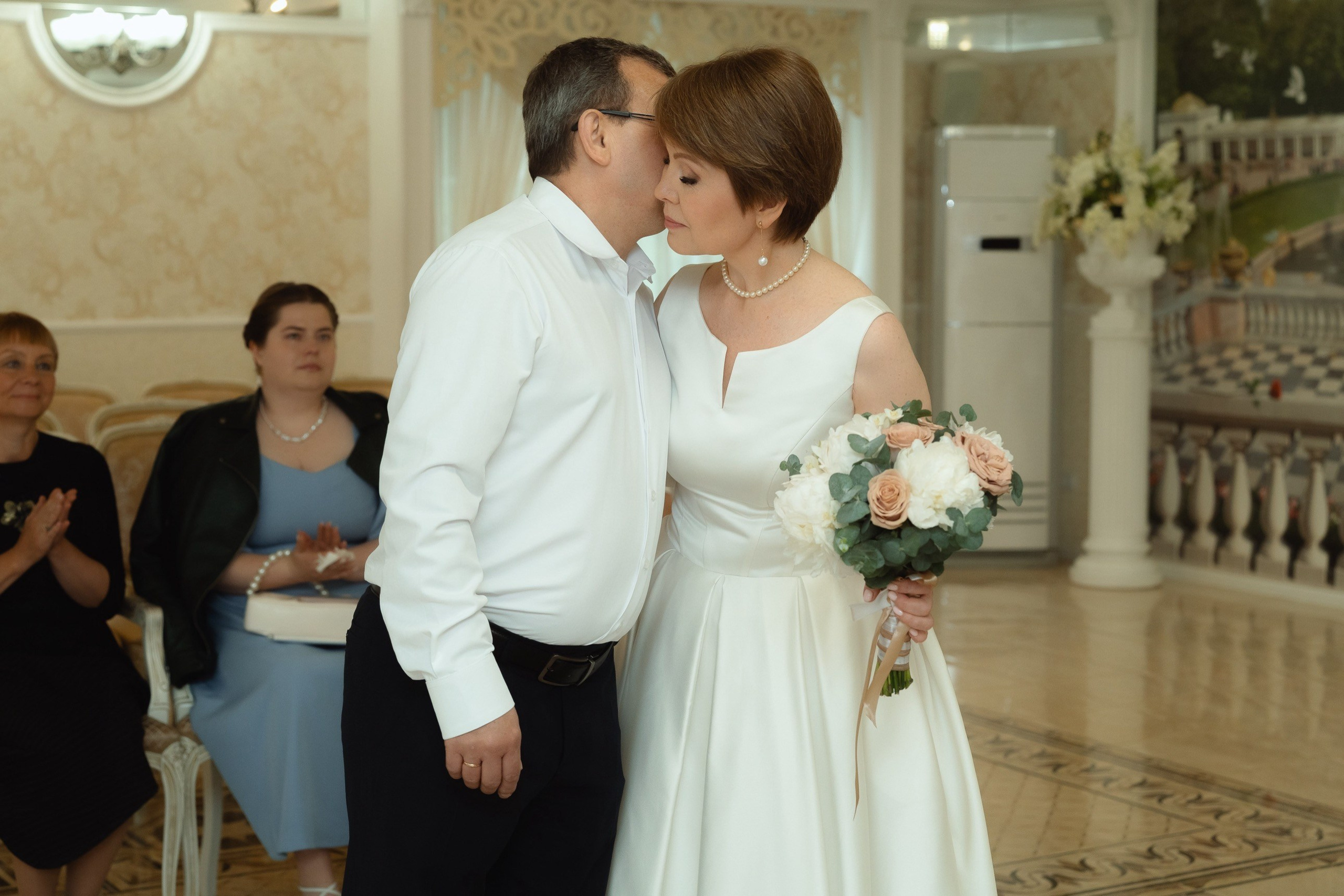 Жених нежно целует невесту в ЗАГСе, букет в руках