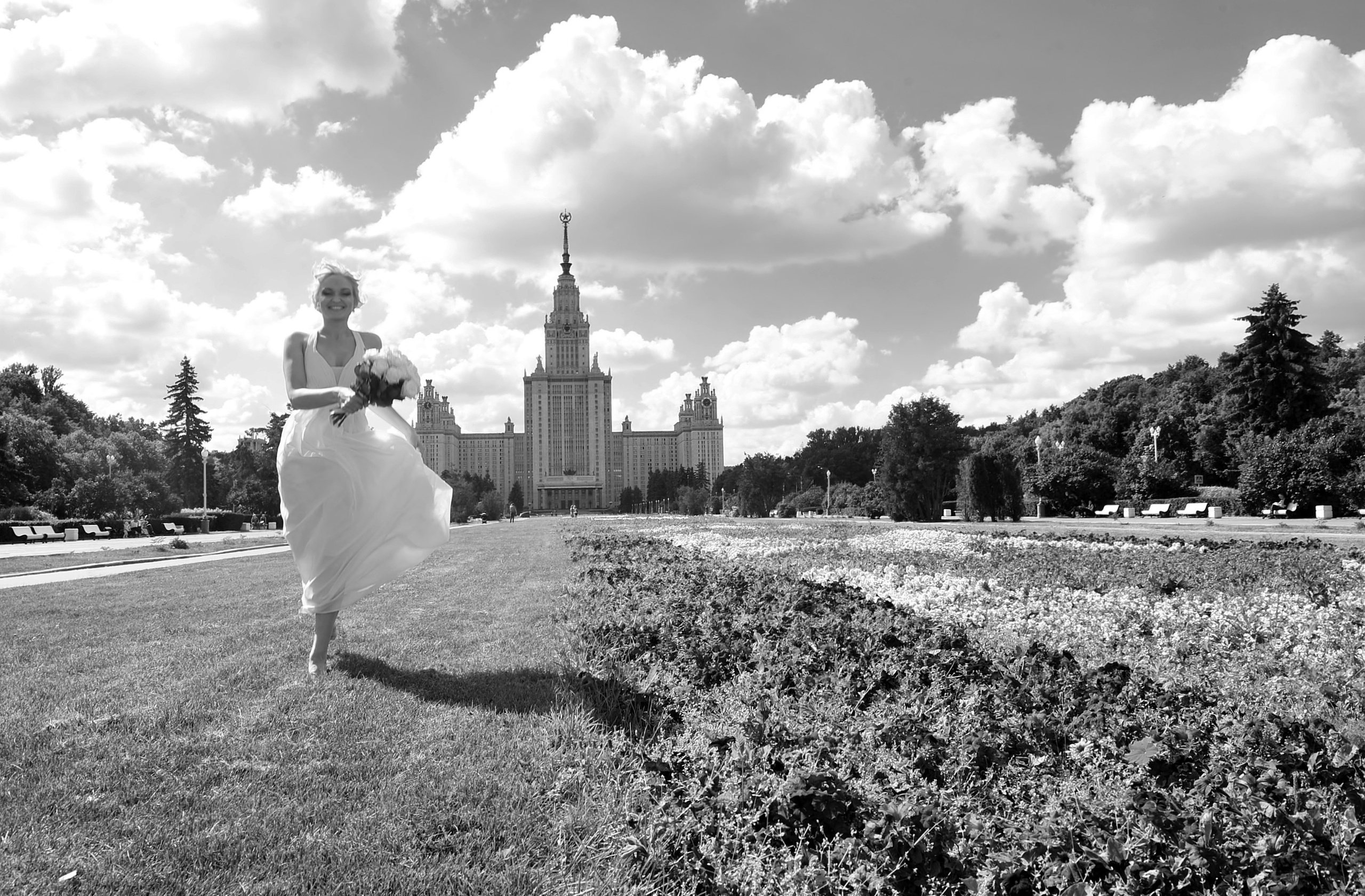 Свадьба на Воробьёвых Горах рядом с МГУ, невеста бежит по траве на фоне МГУ, черно-белая фотография