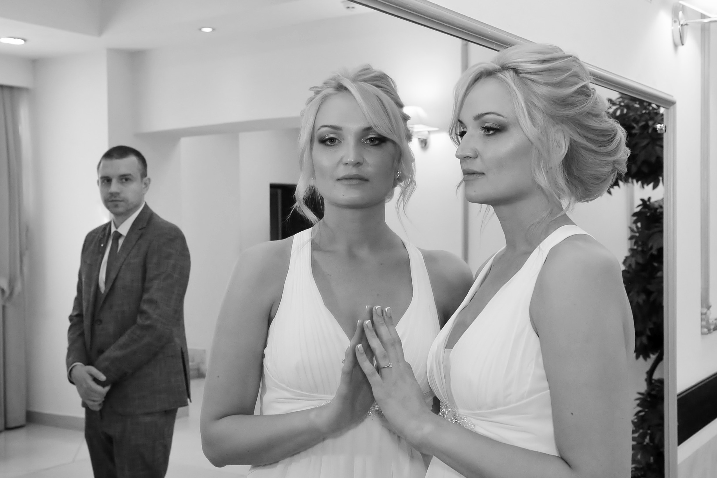 Невеста смотрится в зеркало в ЗАГСе, сзади в зеркале отражается жених, черно-белая фотография