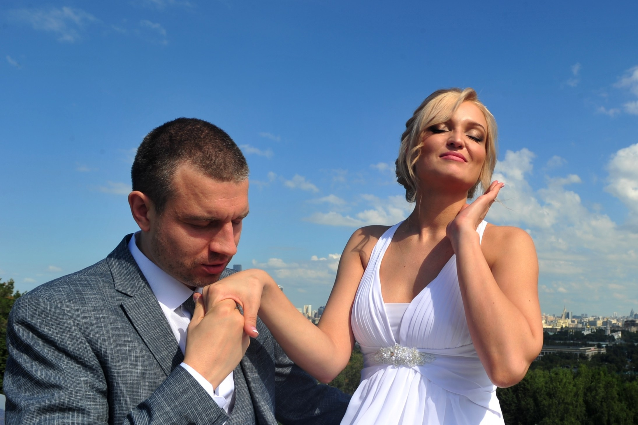 Свадьба на Воробьёвых Горах рядом с МГУ, жених целует руку невесты на фоне голубого неба, смотровая площадка на Воробьёвых Горах