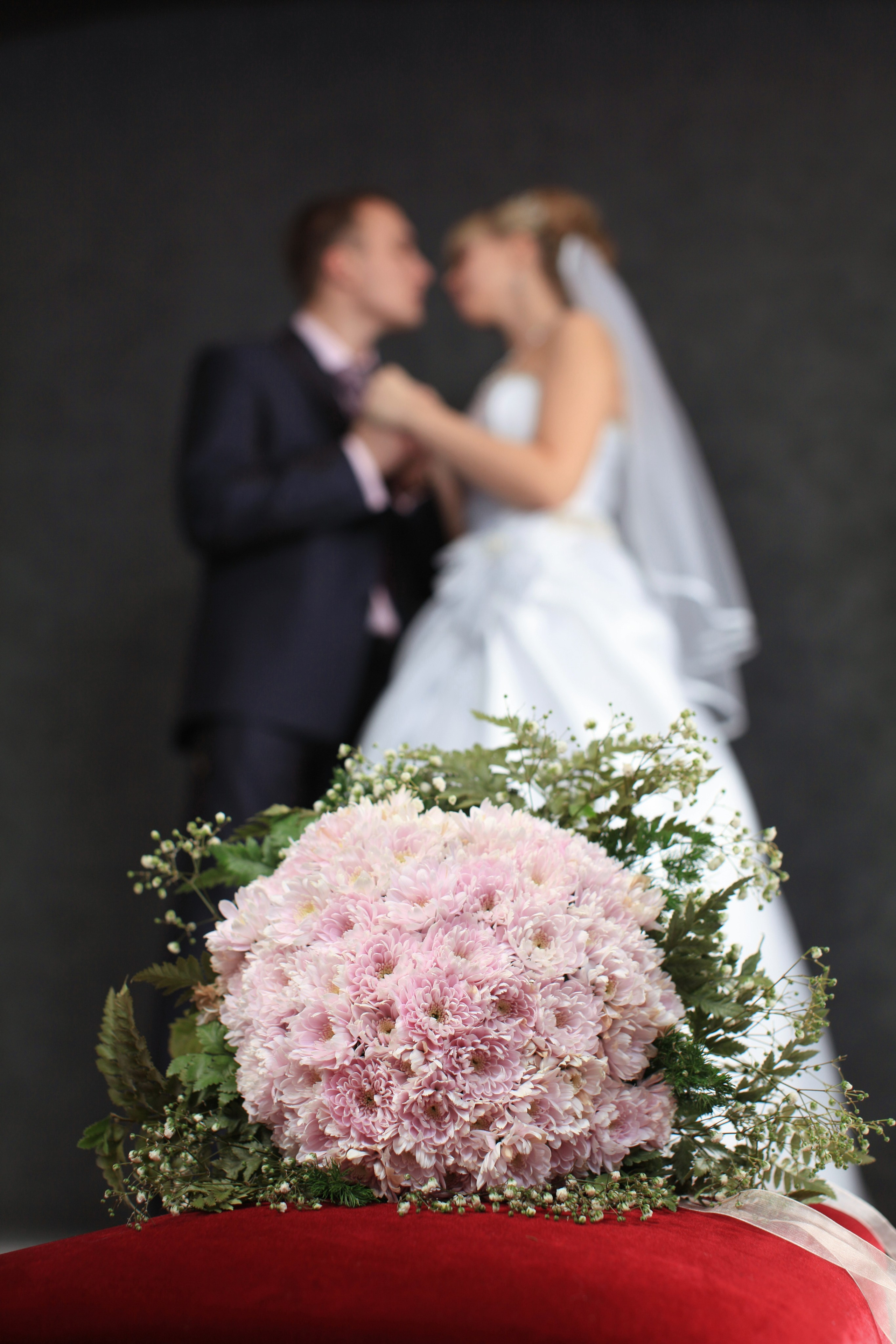 свадебная фотосьемка где невеста держит за руки жениха на темном фоне рядос с букетом цветов 