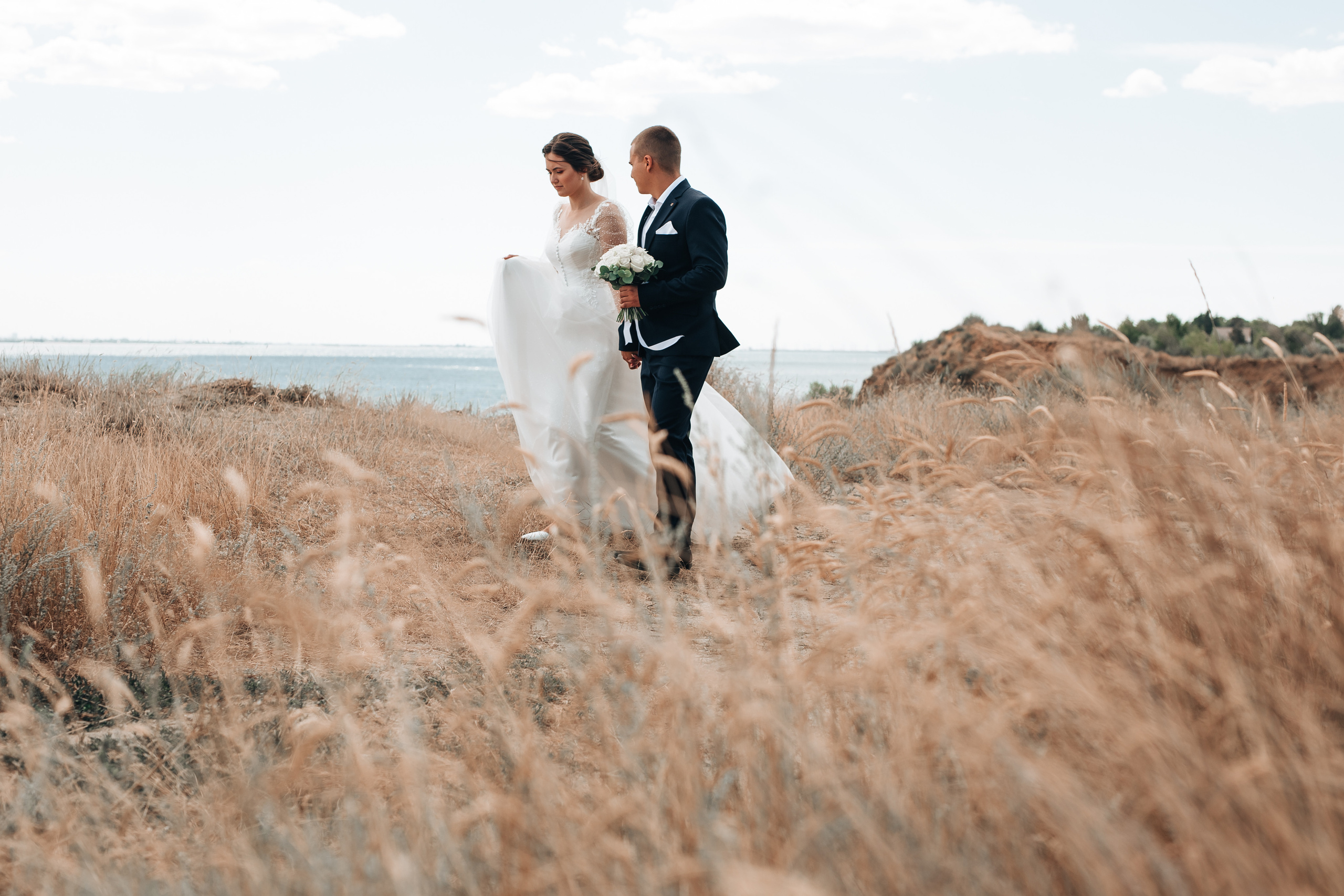 Жених и невеста идут за руку в поле 