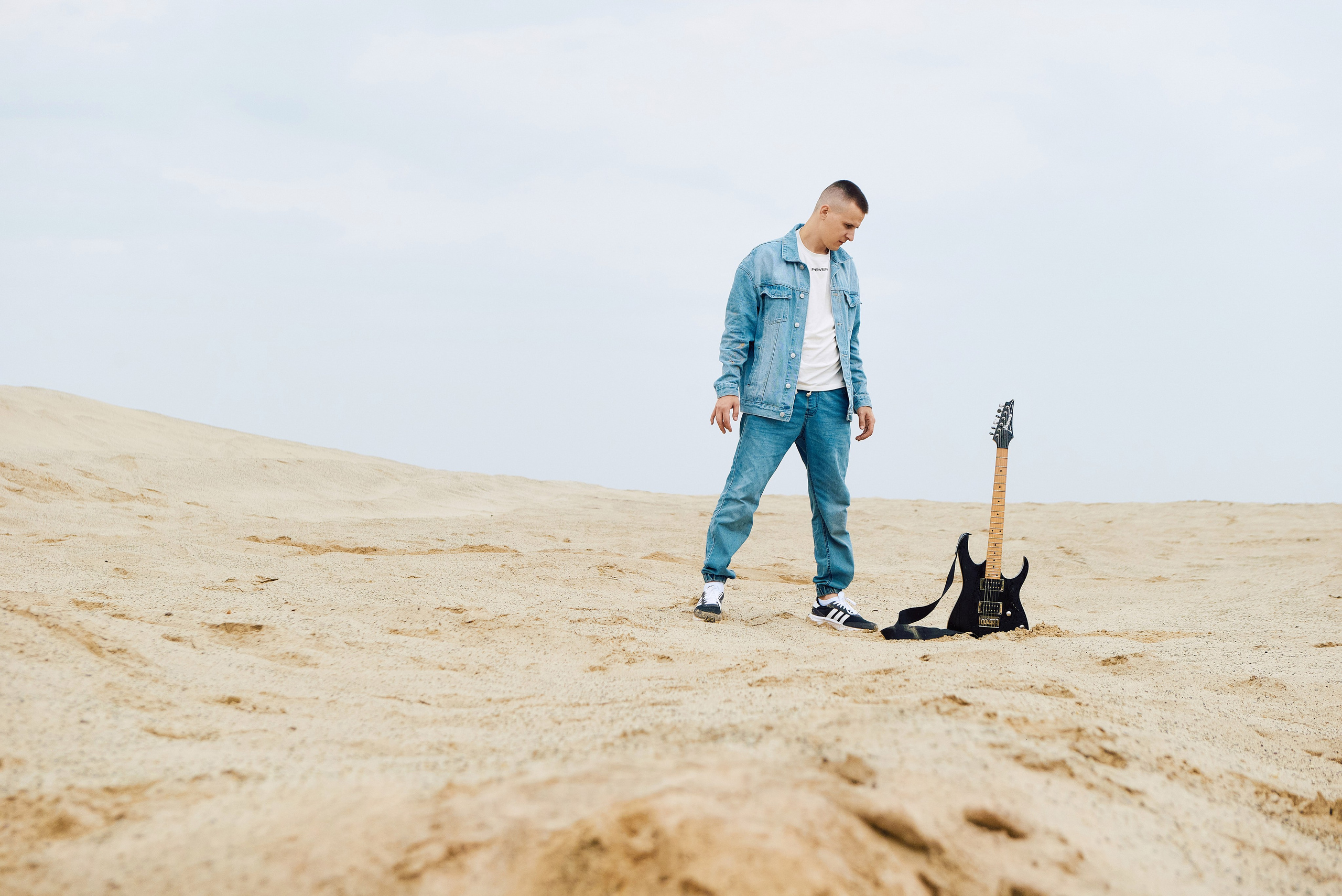Парень в джинсах в пустыне смотрит на гитару