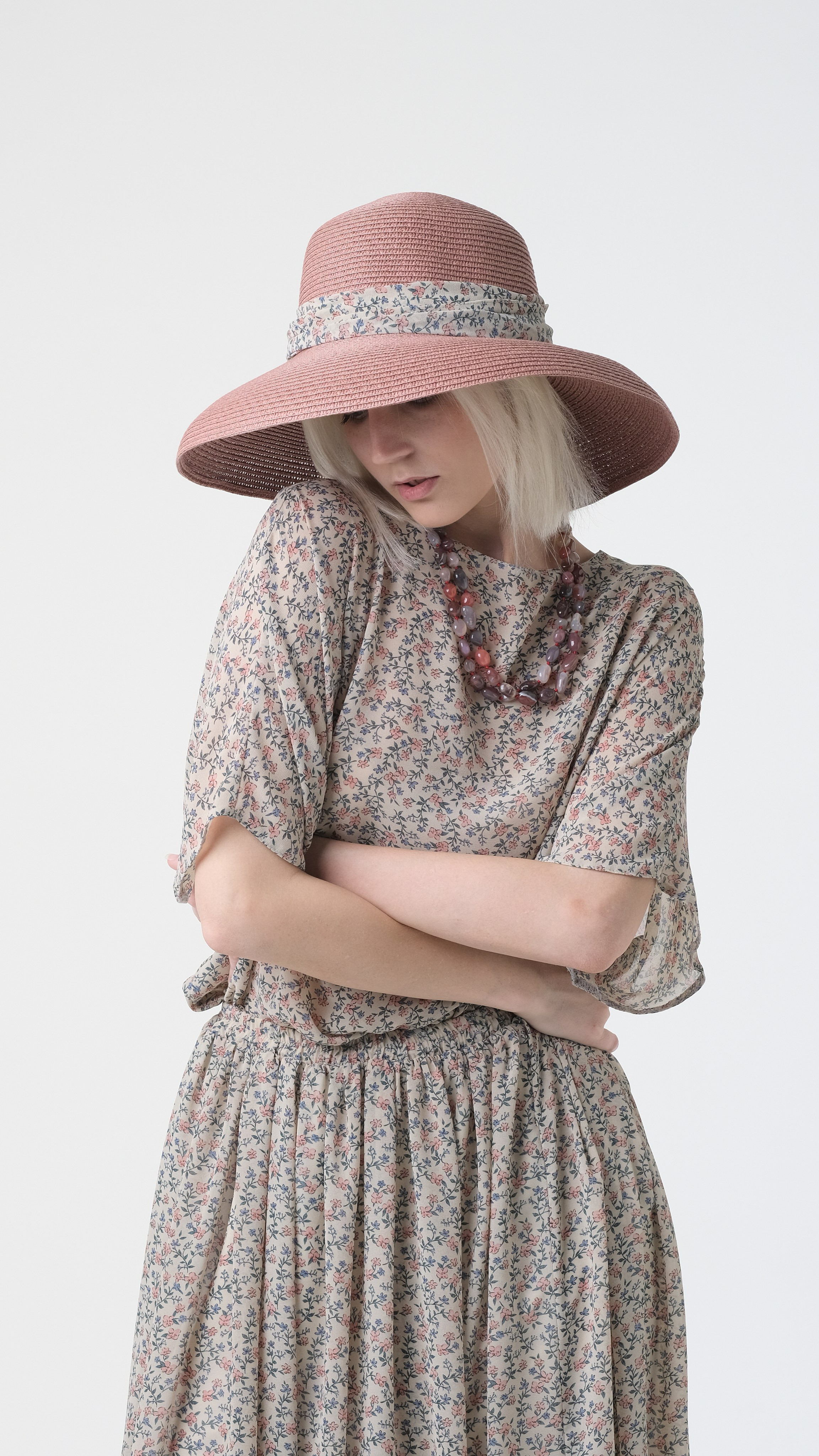 Девушка-модель со сложенными руками. Красивое позирование. Девушка в шляпе и светлом платье. Фотосъёмка на циклораме.