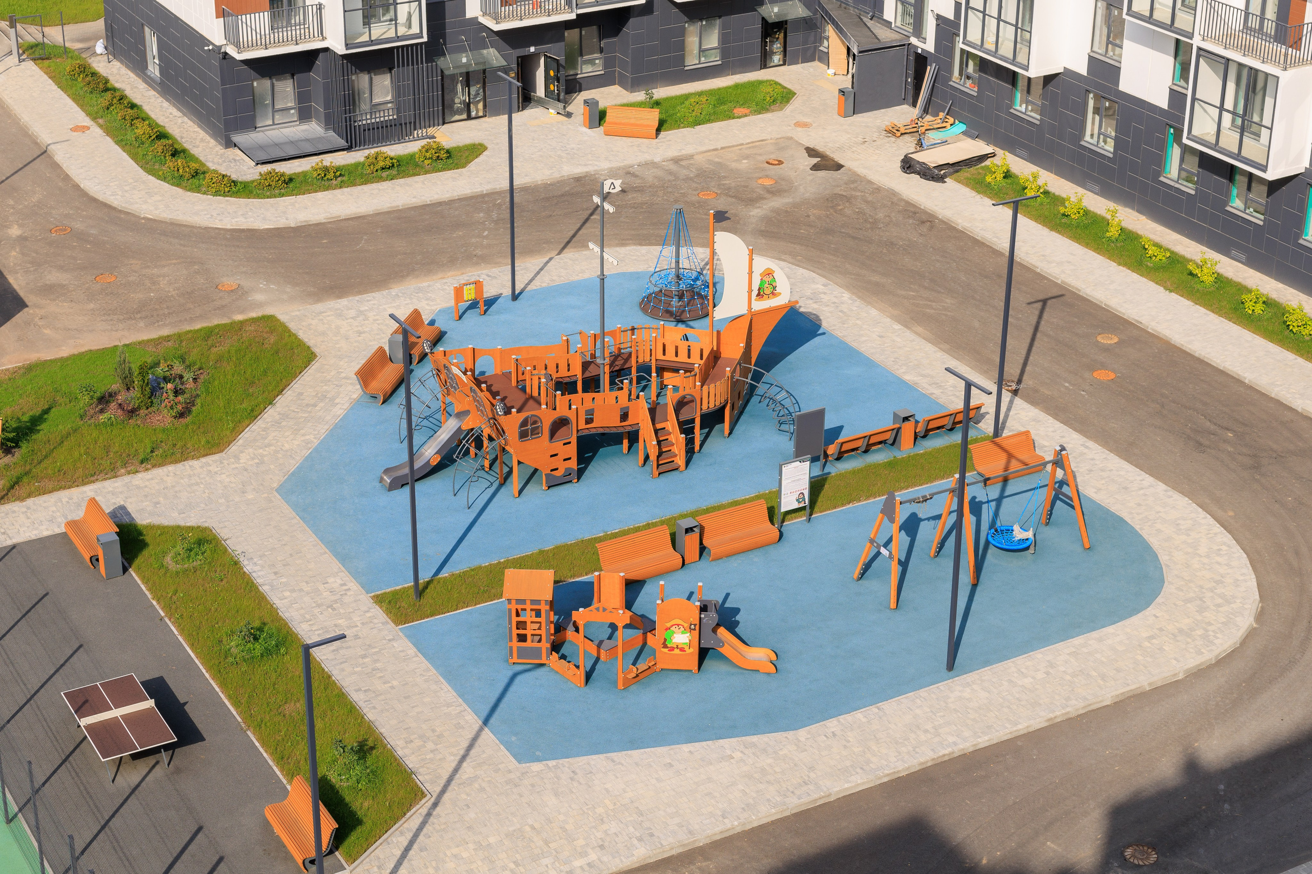 Вид сверху на детскую площадку в форме судна, расположенную во дворе жилого комплекса.