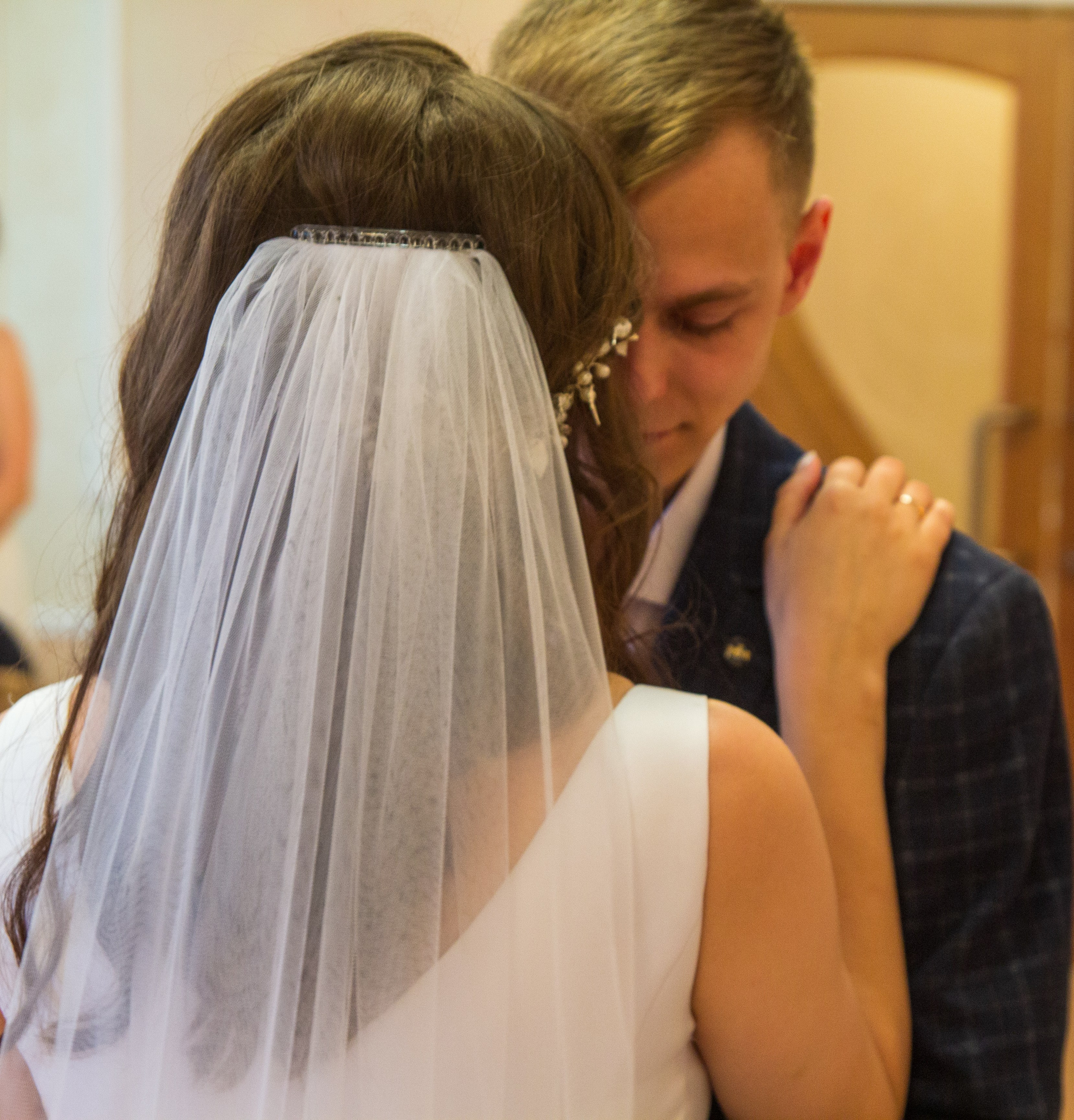 Вид со спины — невеста с фатой обнимает жениха перед регистрацией.