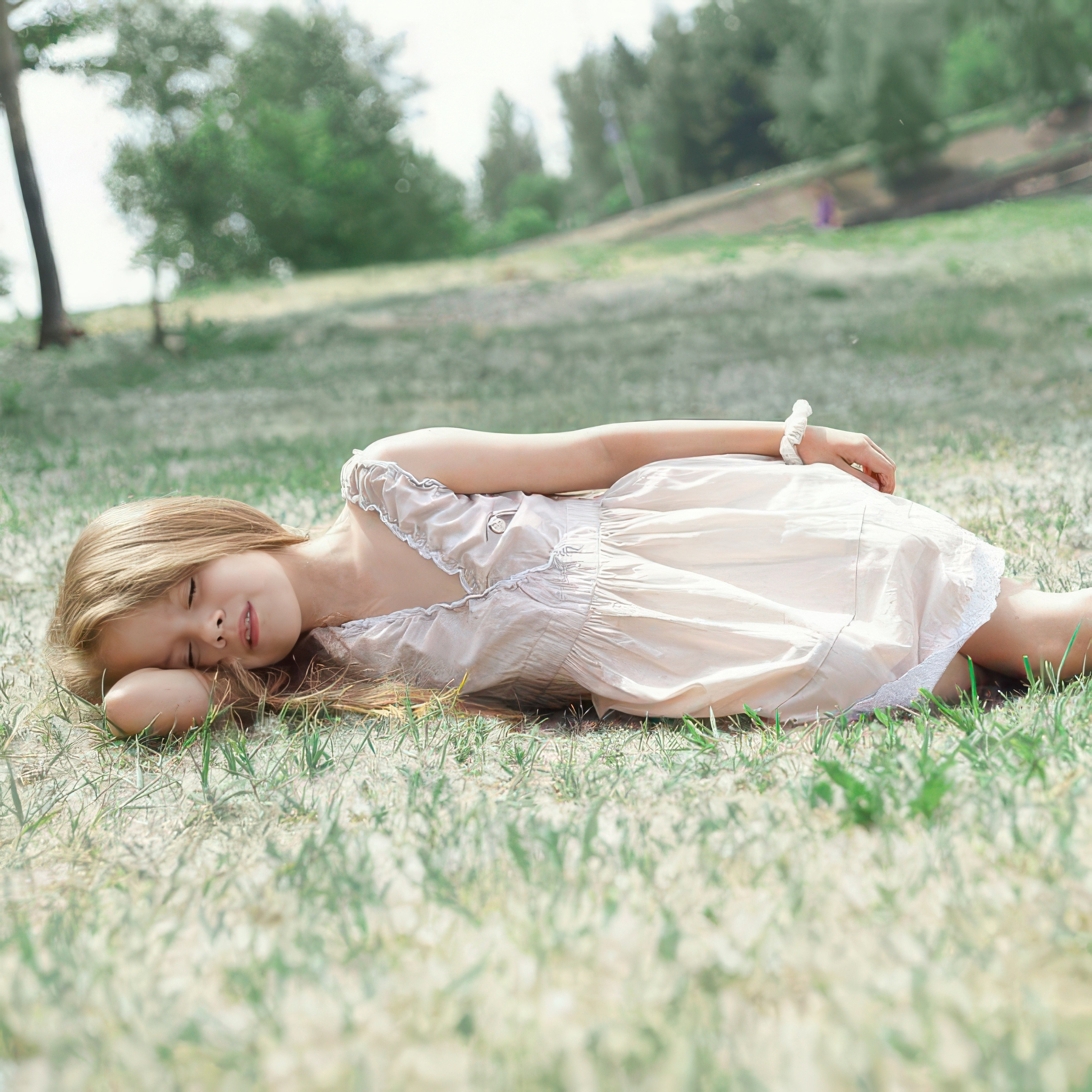 Детская фотосессия летом - девочка лежа на земле с тополиным пухом