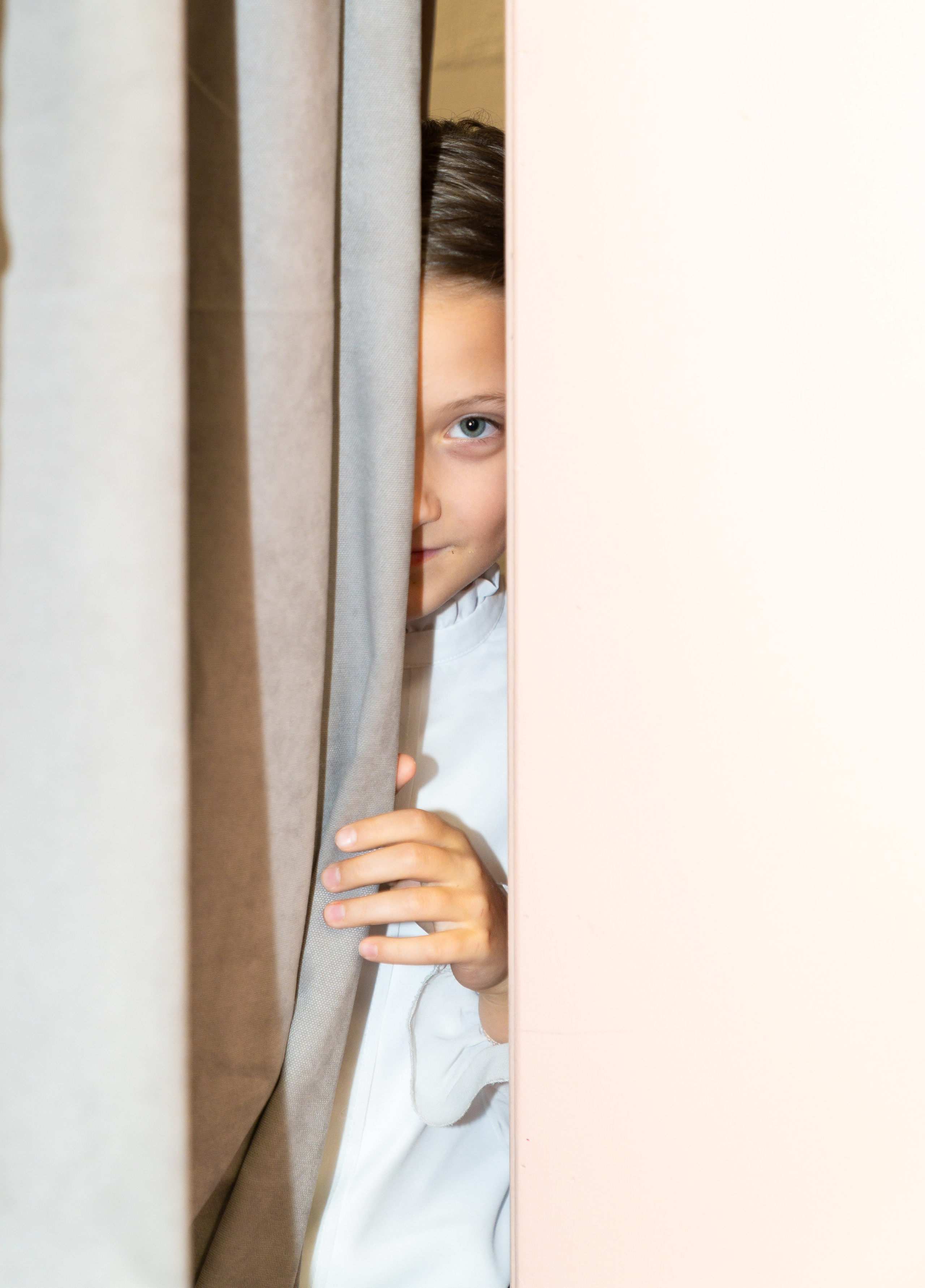 Девочка 7–8 лет выглядывает из-за шторы, любопытный взгляд, портрет ребёнка на детском мероприятии в шахматном клубе Белая Королева, фотограф Евгений Мальцев.