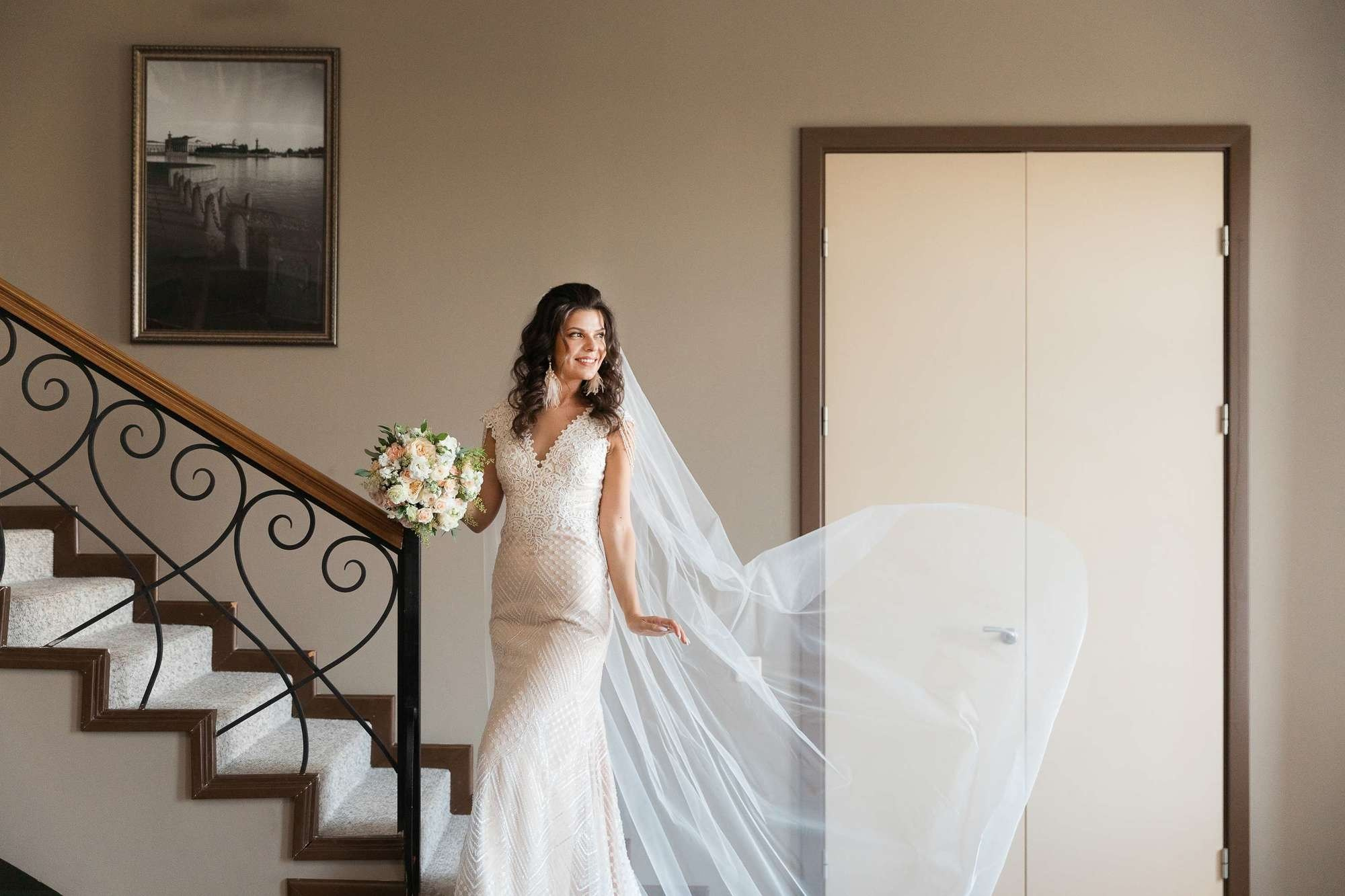 Невеста с фатой и букетом у лестницы дома