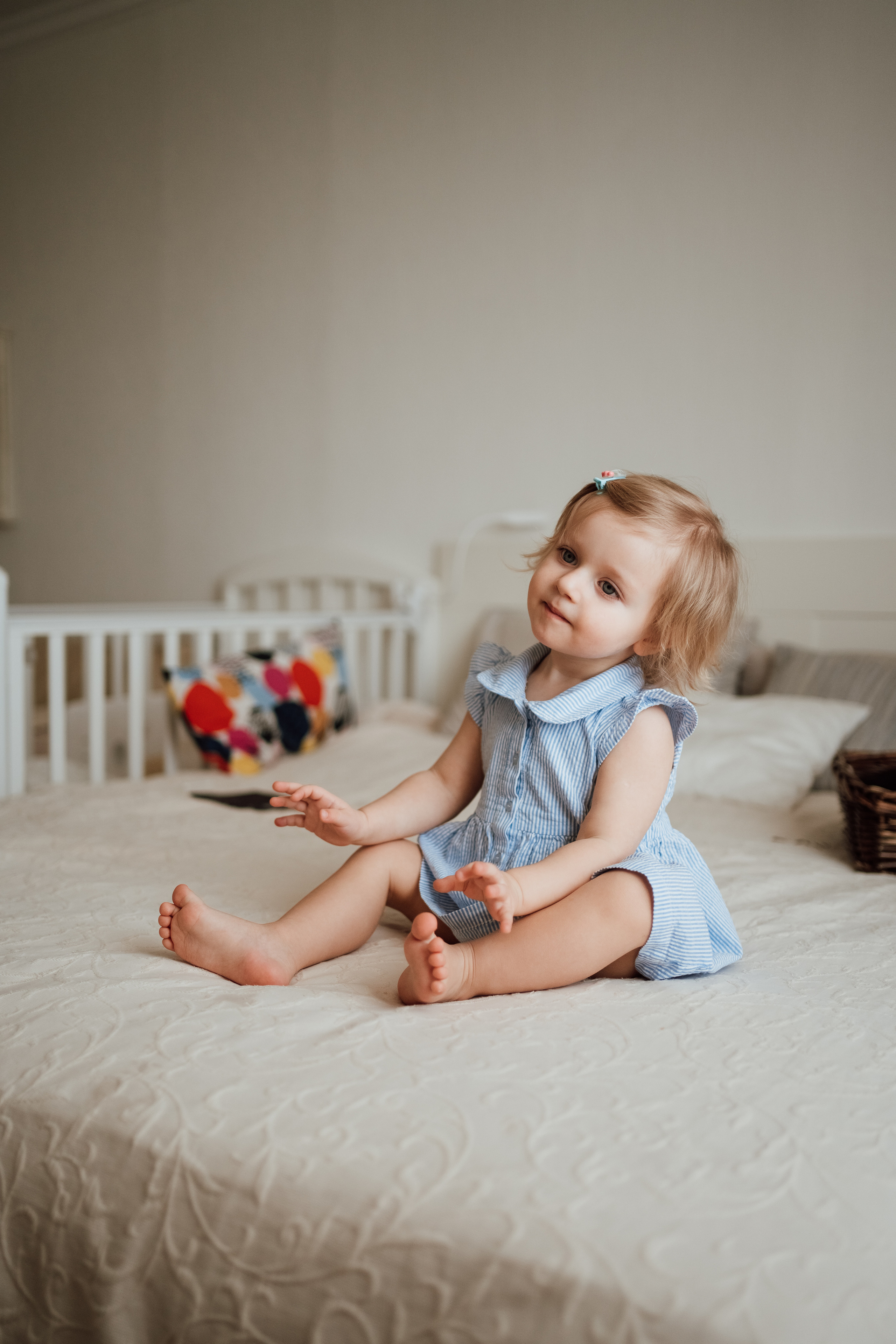 Маленькая девочка в голубом платье сидит на кровати
