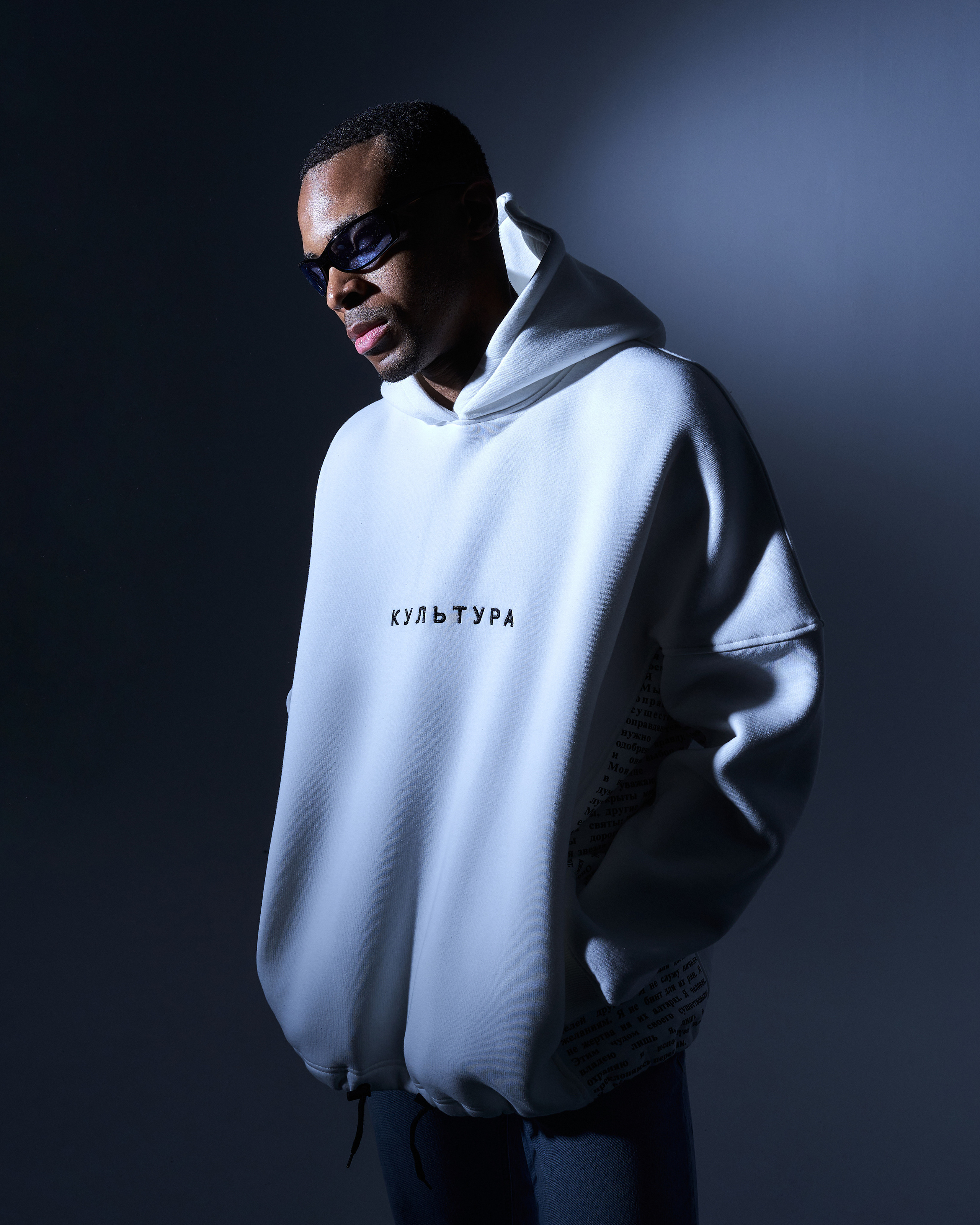 Темнокожий мужчина в белом oversize худи на сером фоне