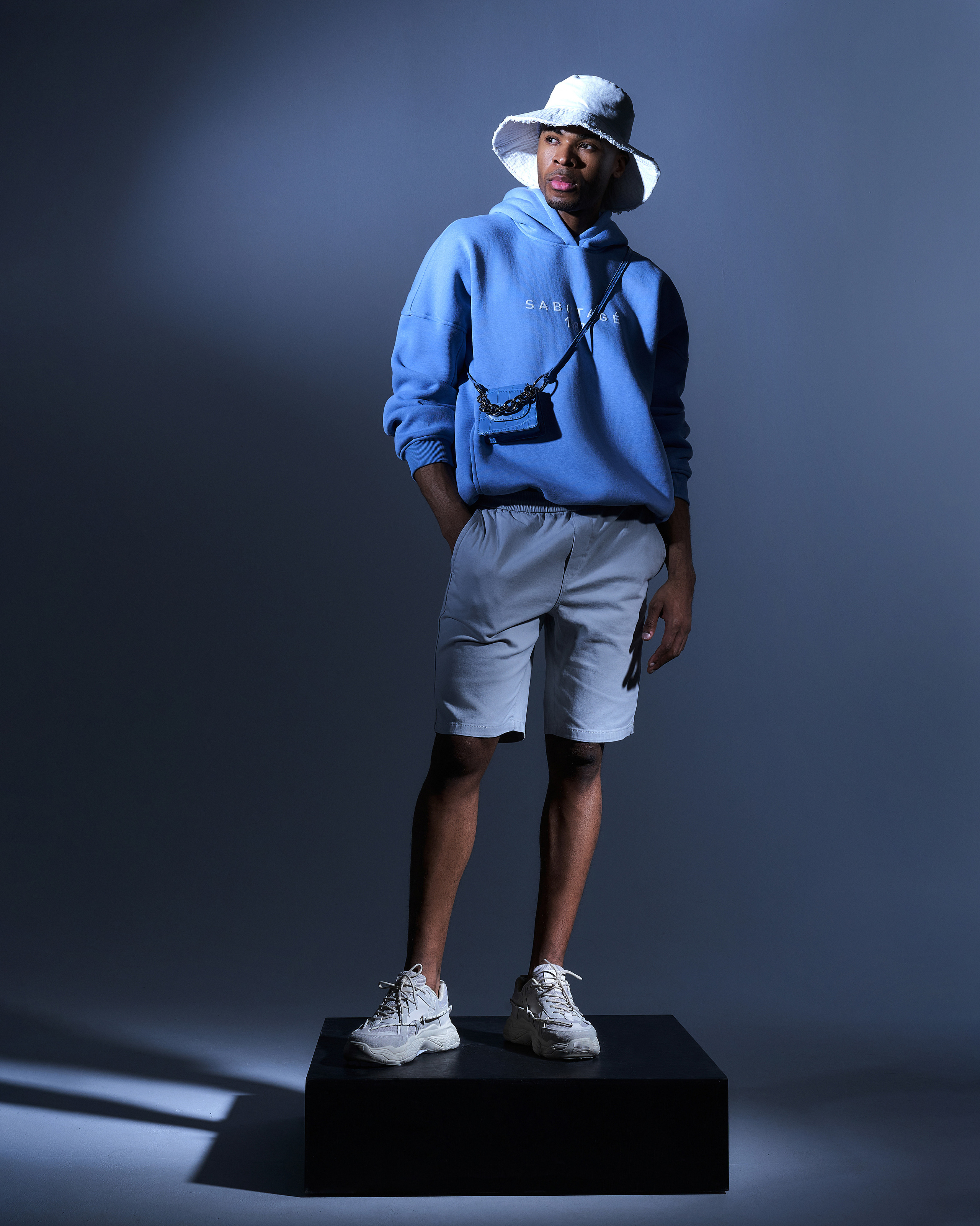 Стильный темнокожий парень модель в голубом худи и панаме в креативной съемке