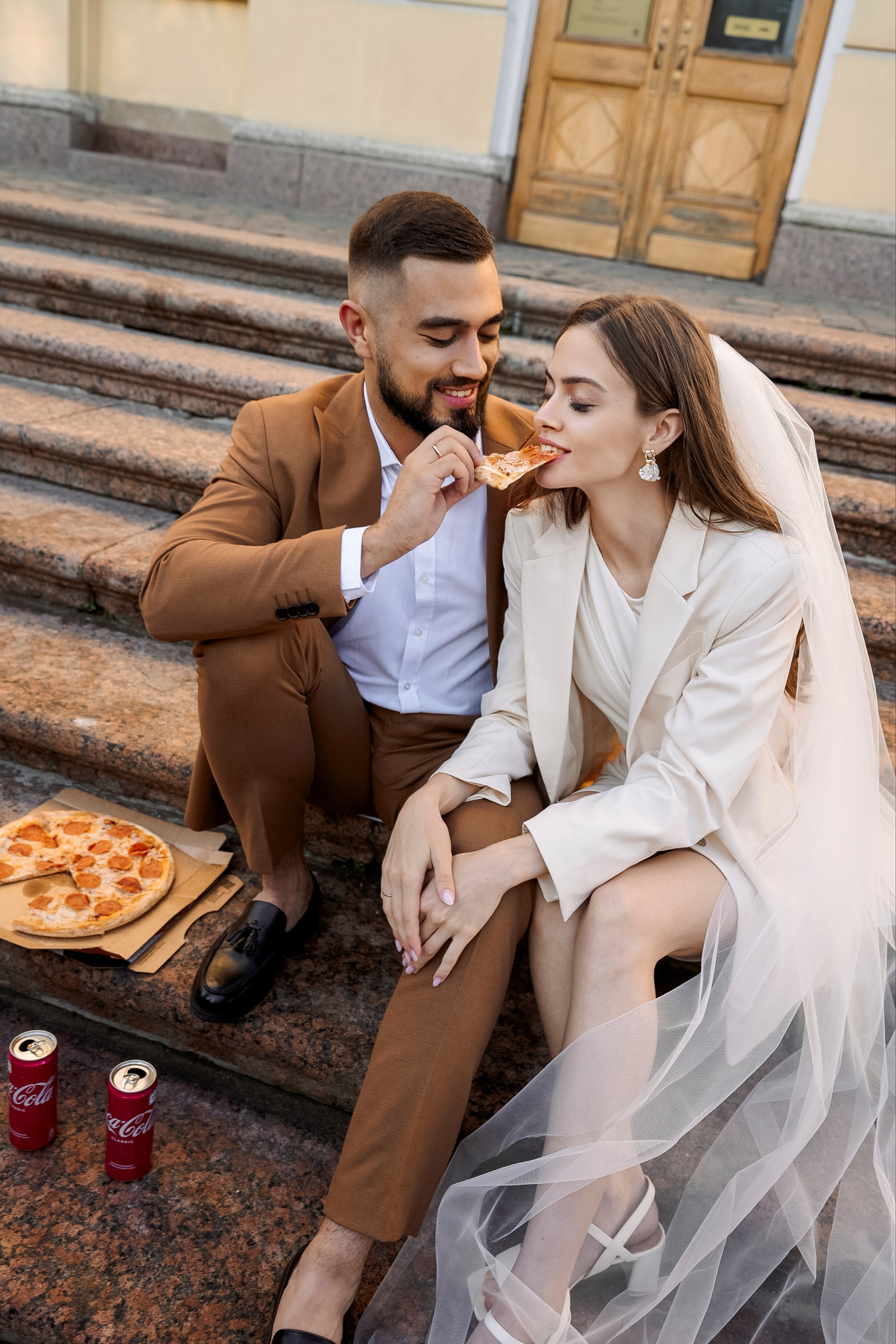 Жених и невеста сидят на ступенях и едят пиццу