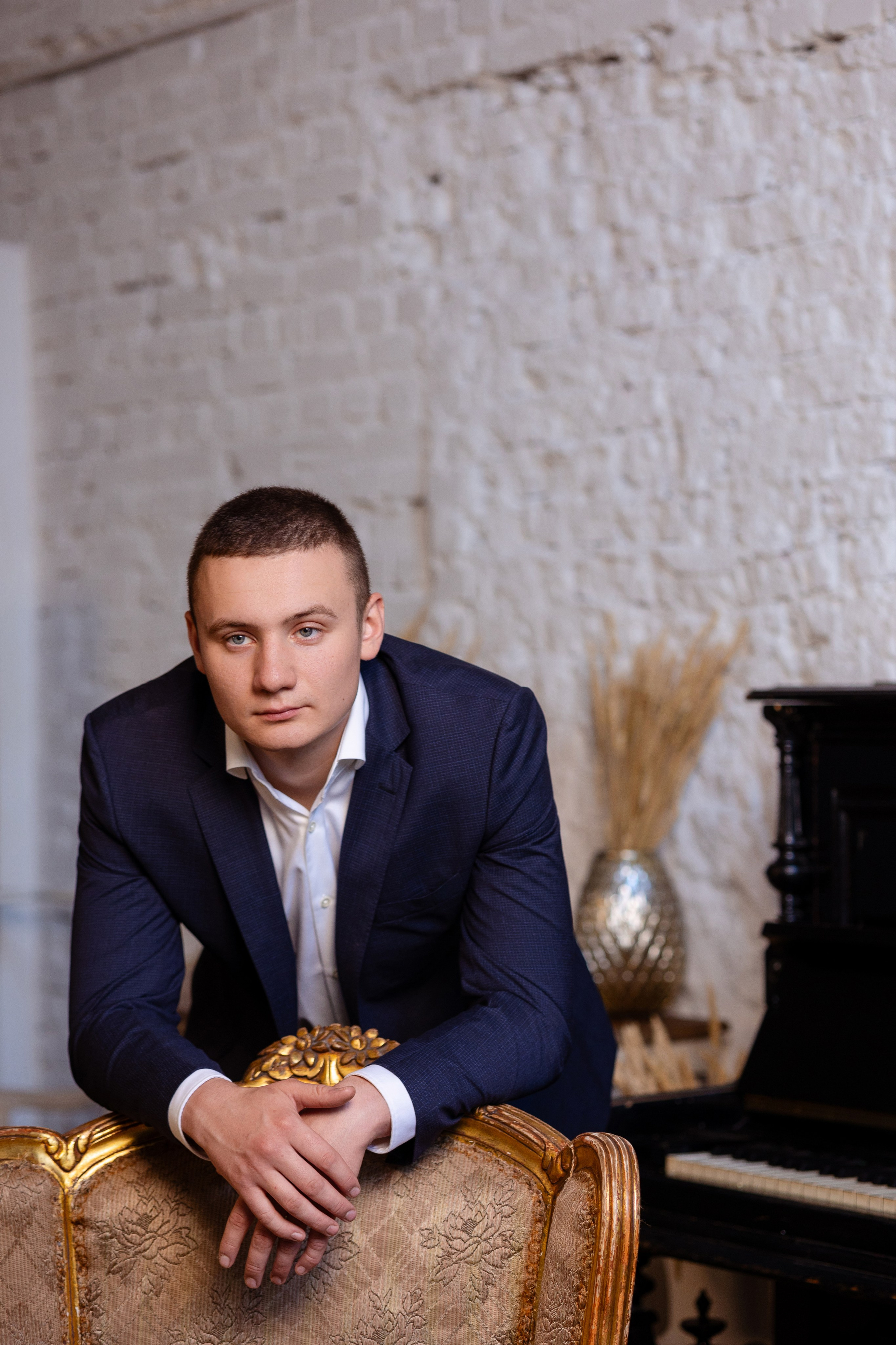 Жених стоит за стулом, облокотившись на него.