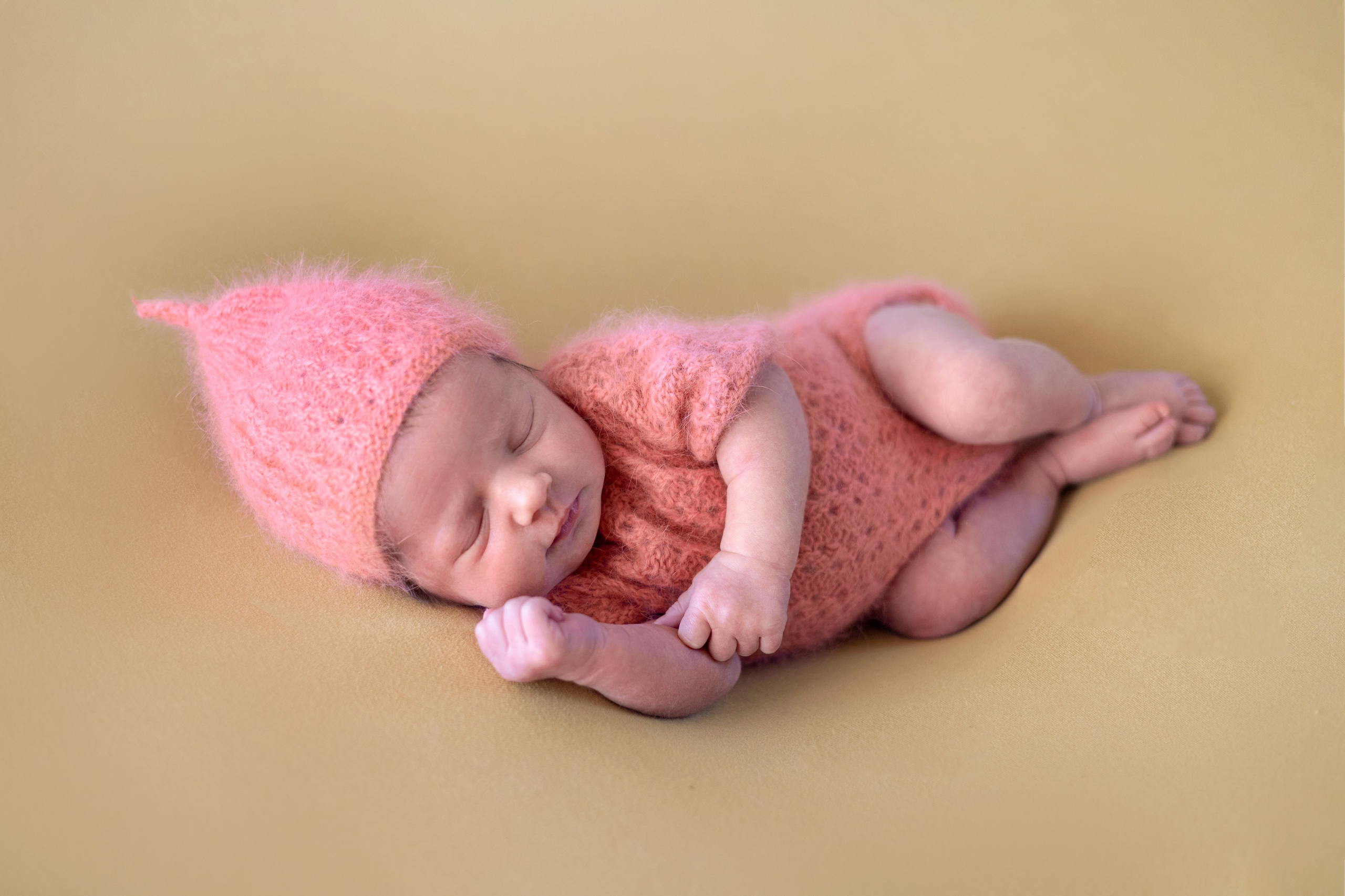 новорожденная девочка спит на боку в пушистом наряде персикового цвета