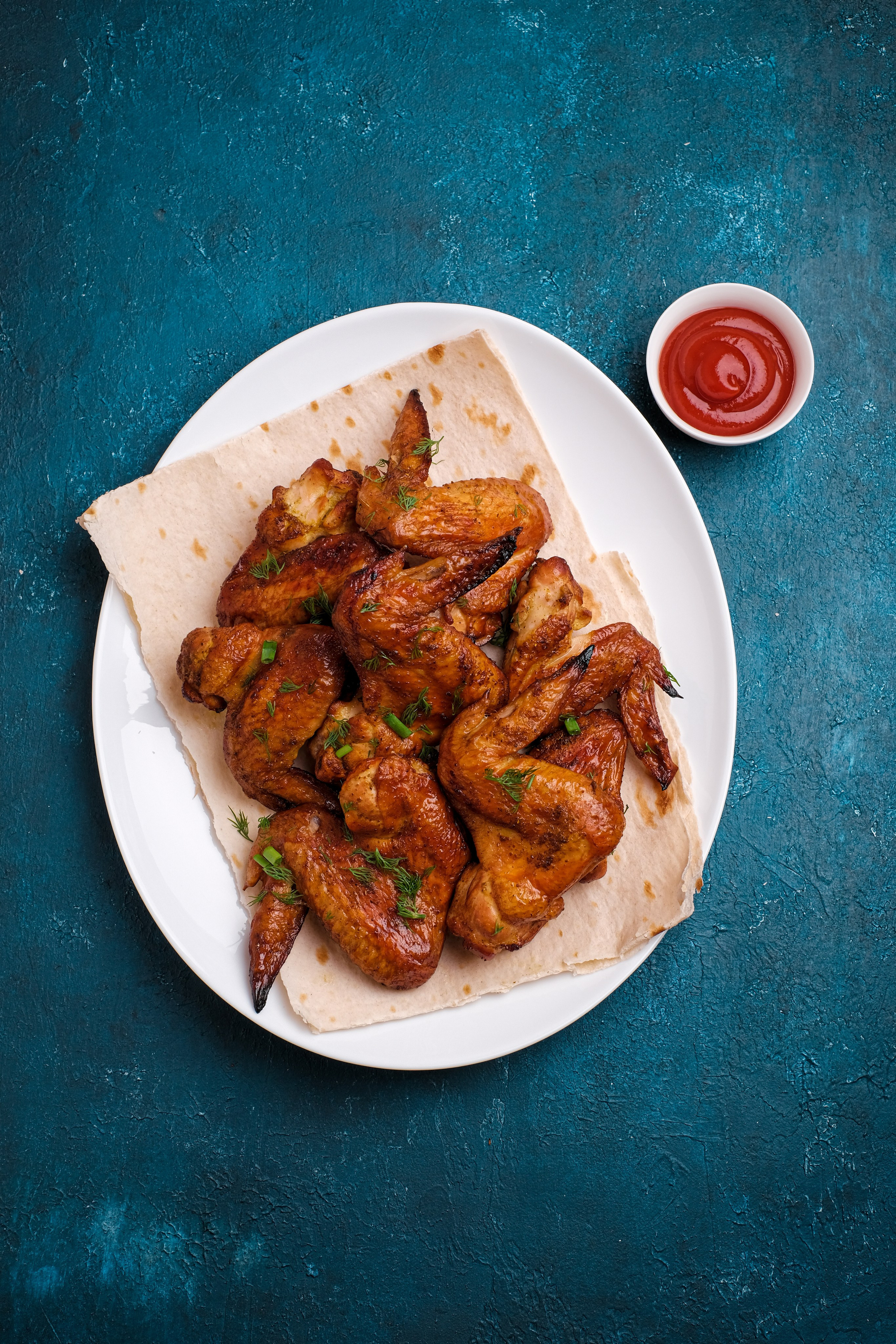 Фотография тарелки с жареными крыльями барбекю на синем фоне. фуд-фотография для меню кафе в Красноярске.
