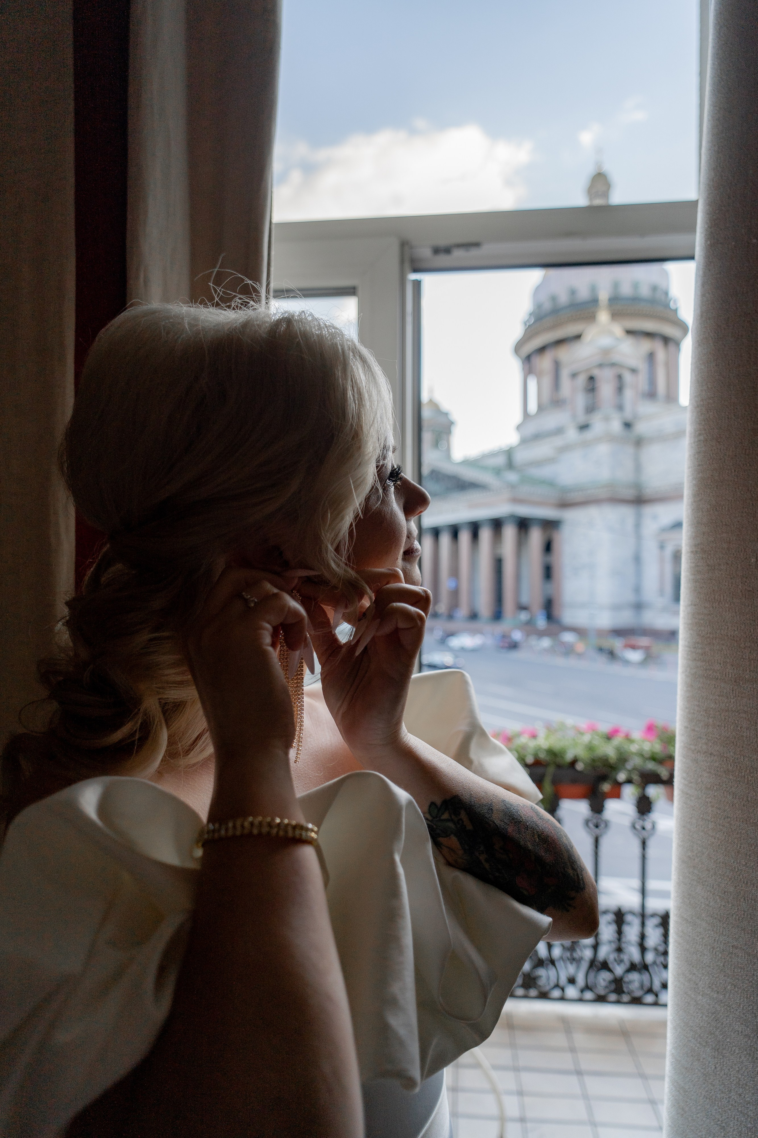 Невеста надевает сережки и смотрит на Исаакиевский собор из окна отеля
