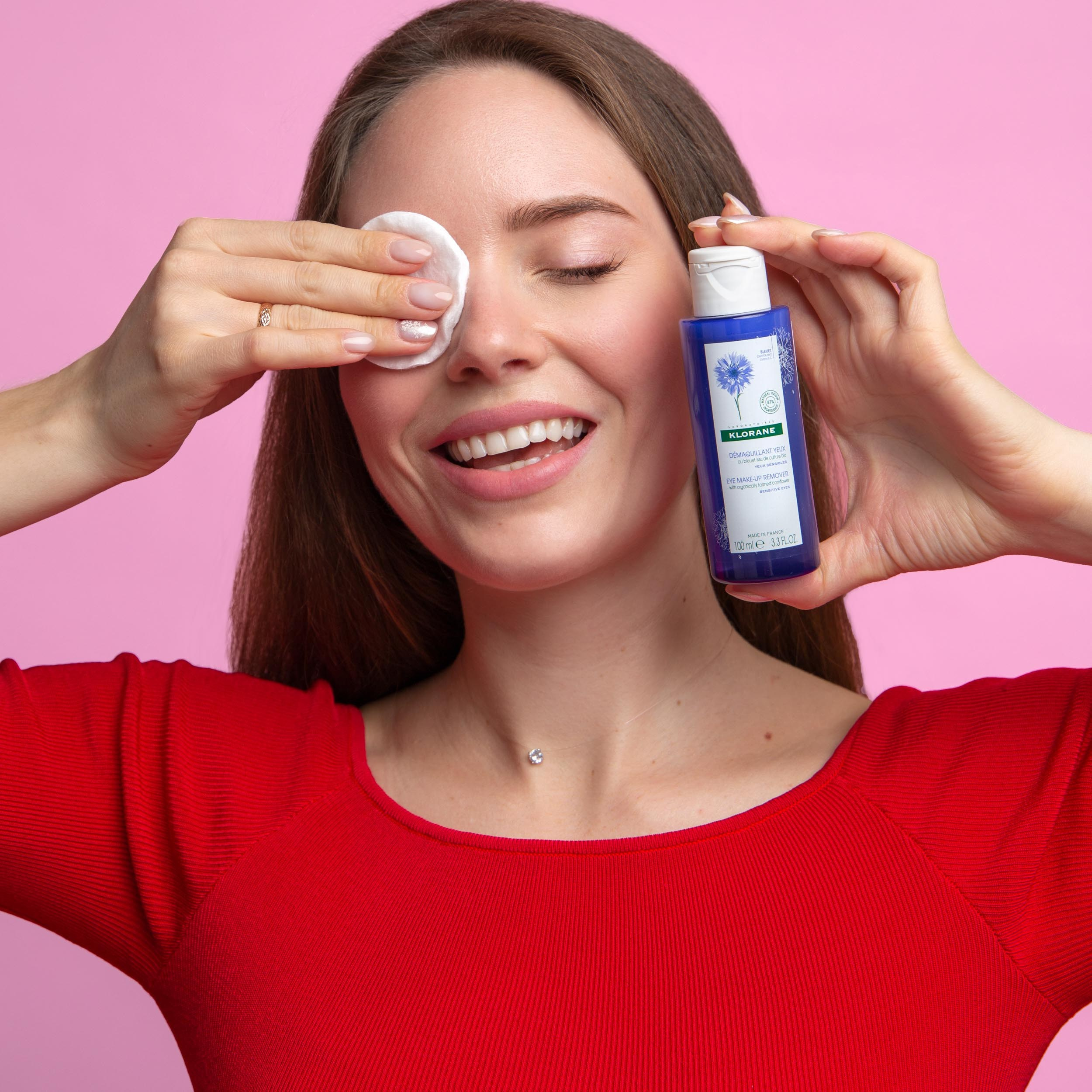 Девушка в красной кофте смывает косметику ватным диском