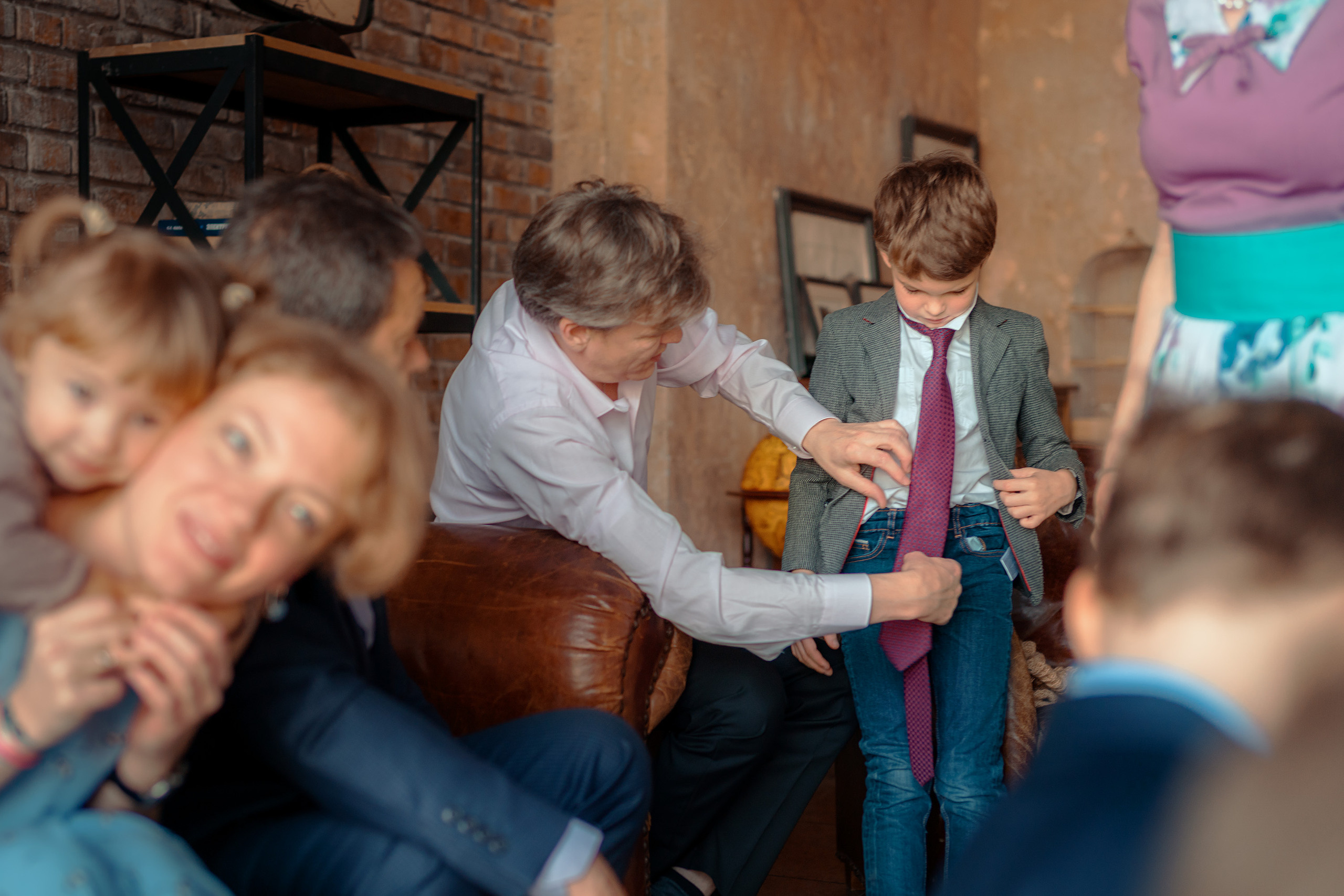 Папа поправляет сыну галстук на фоне других членов семьи