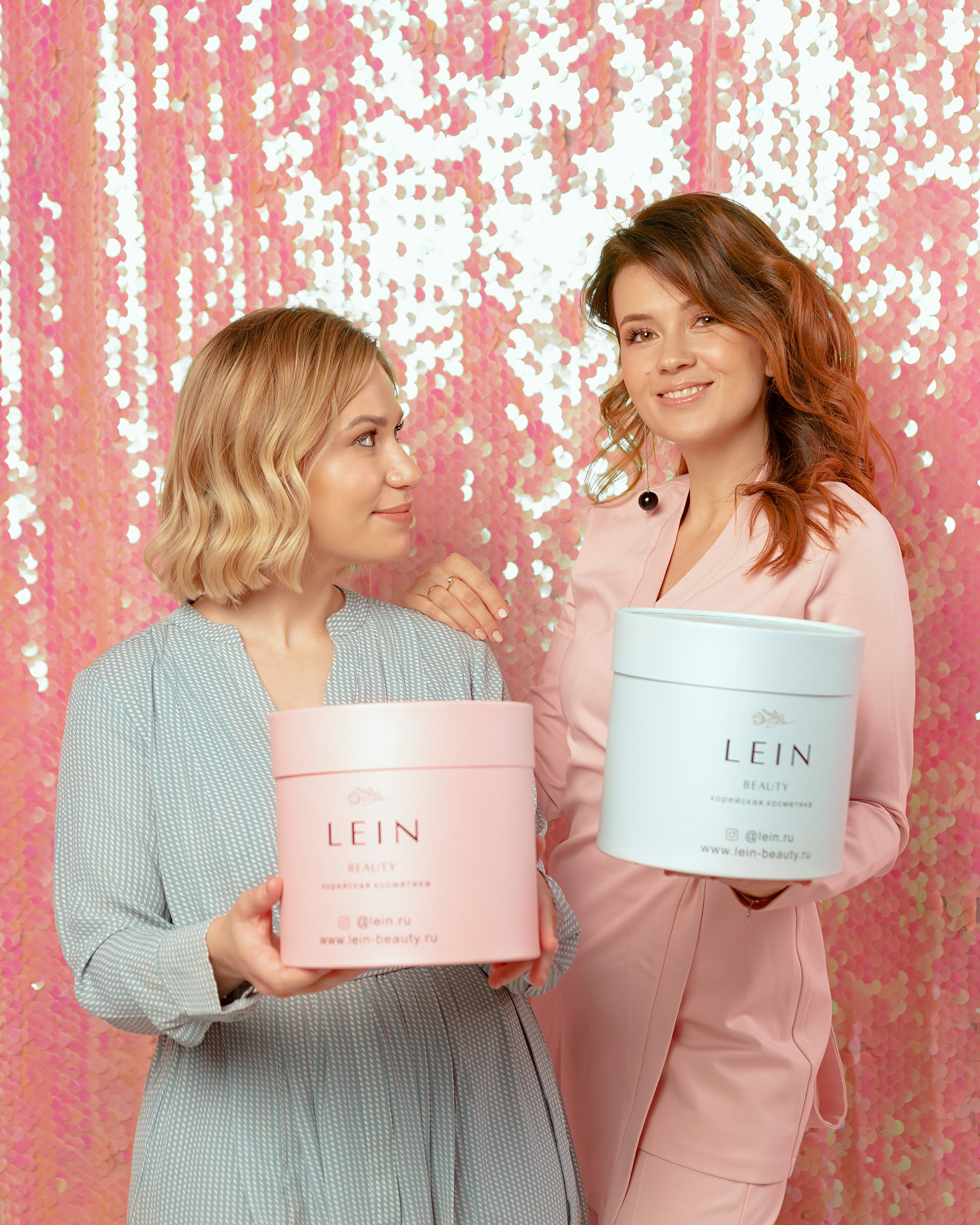 Две девушки рекламируют коробки с косметикой на розовом фоне