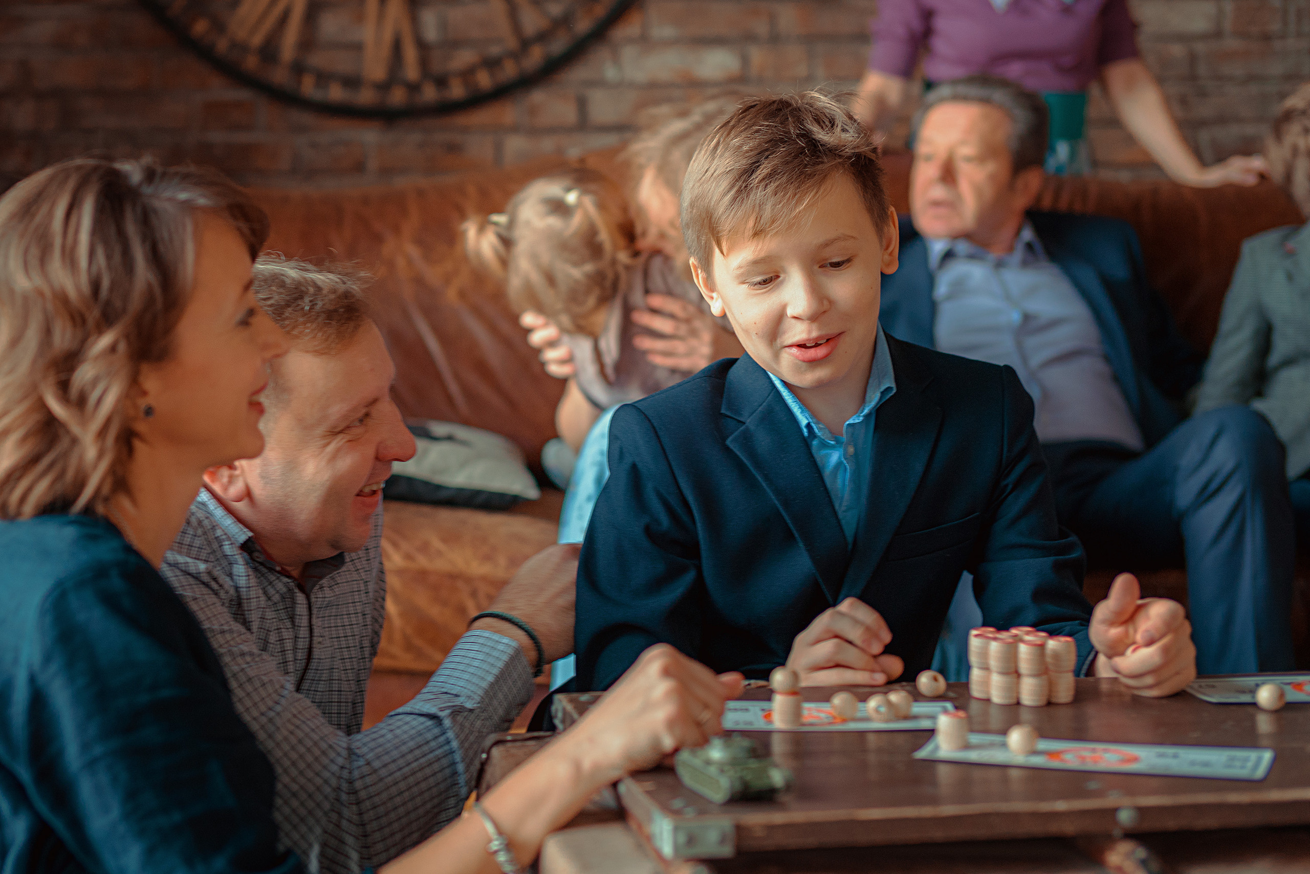 Мальчик с родителями играет в лото на переднем плане, на заднем другие члены семьи общаются на диване