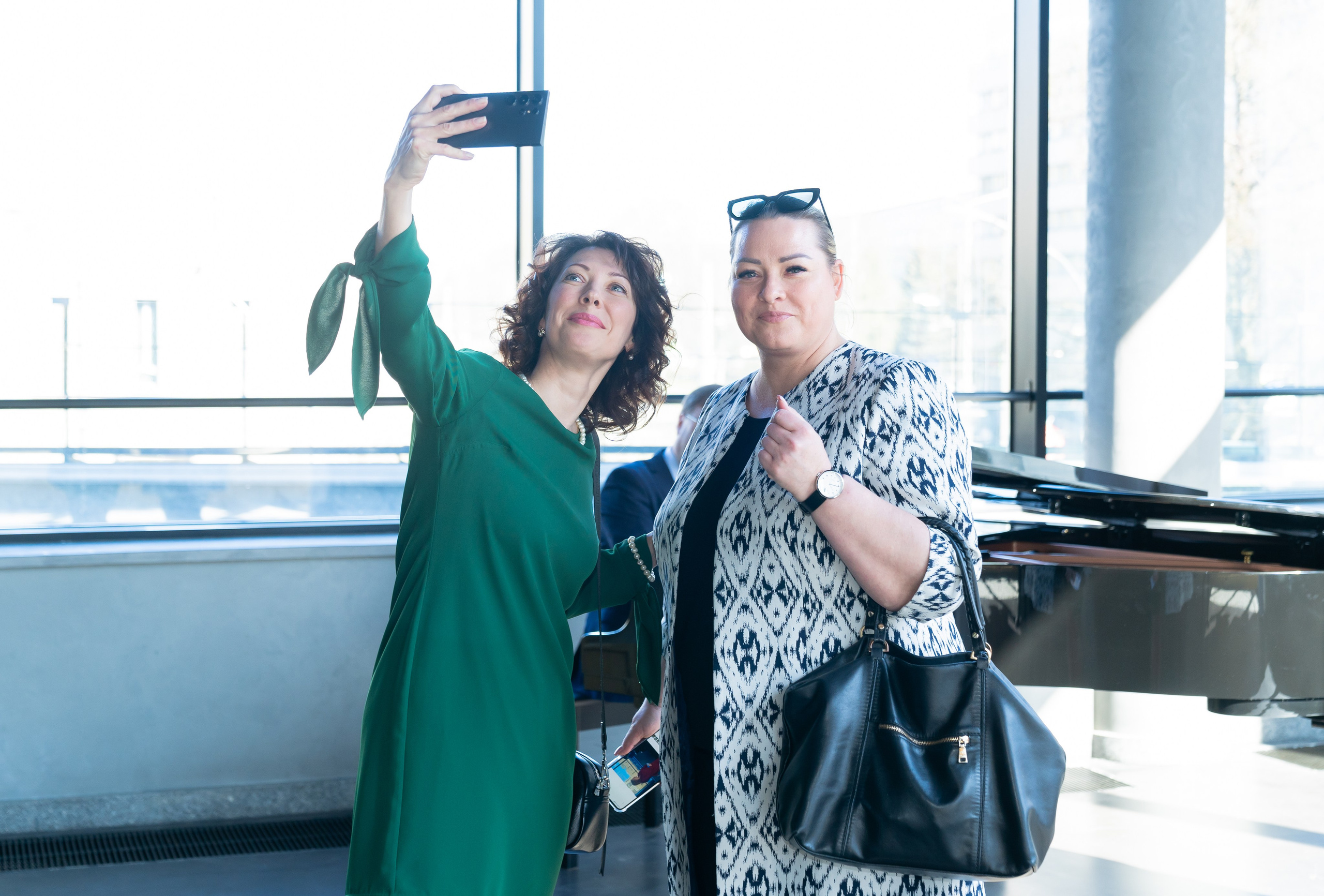 Гости Дня местного самоуправления делают селфи в Центре Курёхина. Женщины в зелёном и узорчатом платье. Фотография Евгения Мальцева.