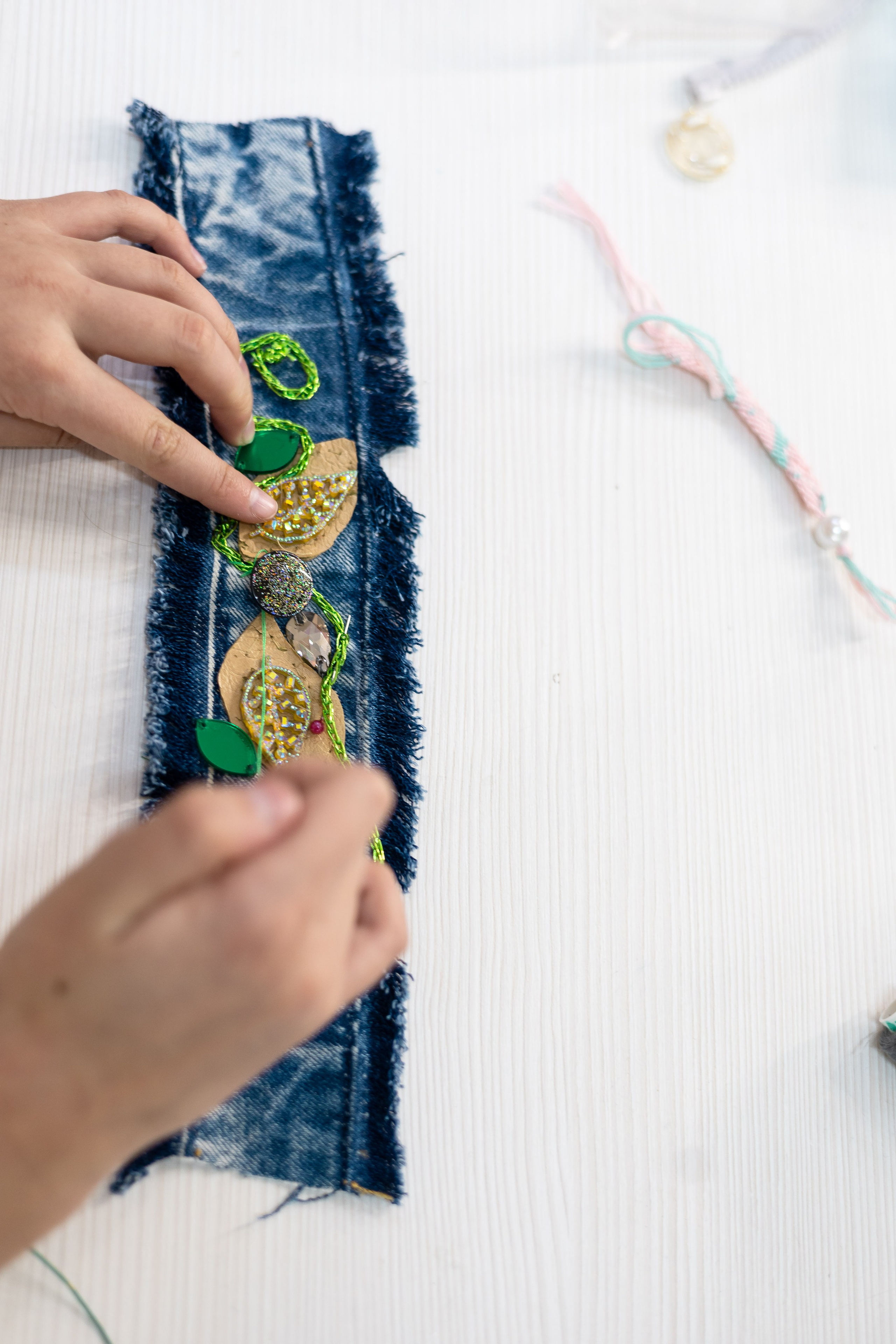 Детские руки примеряют элементы декора на будущий браслет из джинсовой ткани.