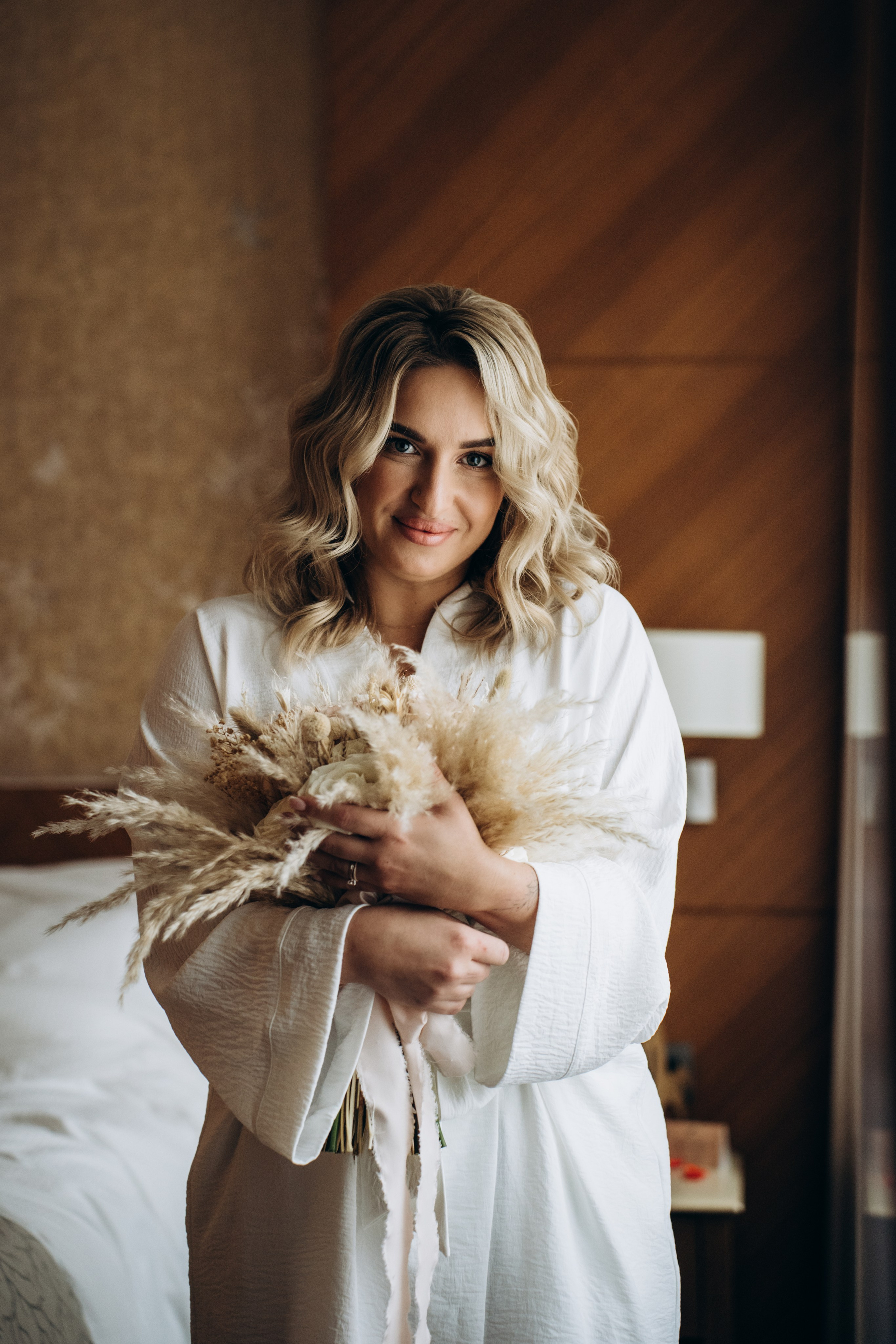 Невеста улыбается, держась за букет — эмоциональные моменты сборов, наполненные ожиданием и радостью.