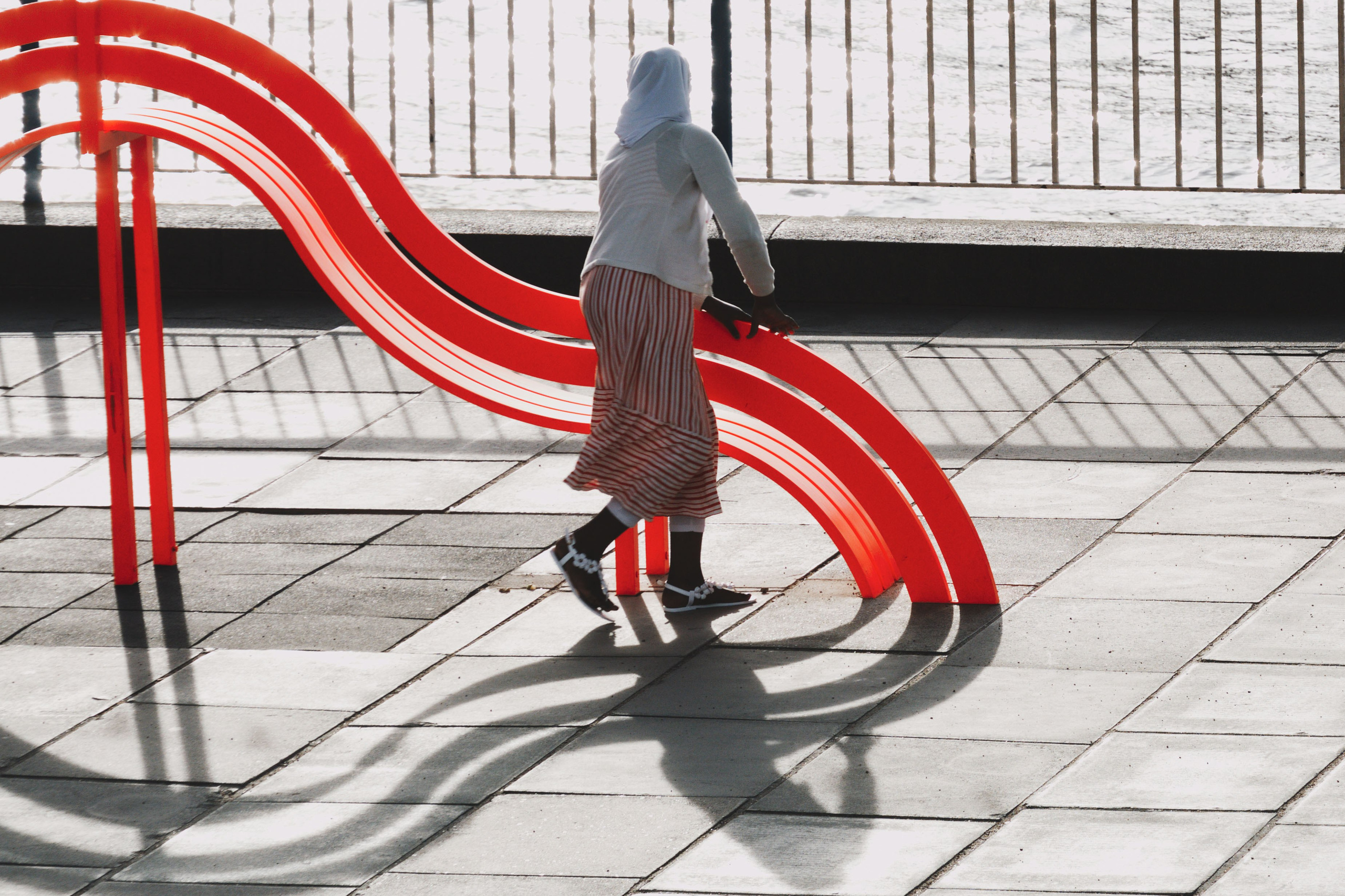  Силуэт человека на фоне красной изогнутой инсталляции, игра света и тени, геометрическая композиция, акцент на текстуре мощения.