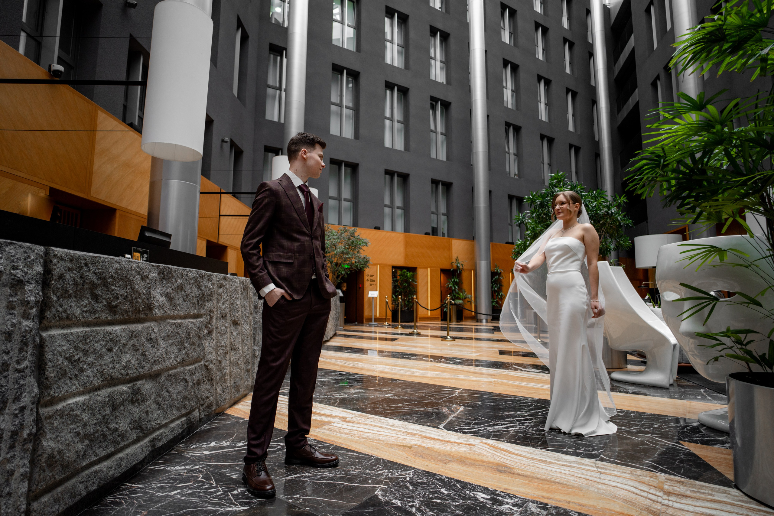 Невеста и жених стоят в главном атриуме в отеле Гамма на свадебной фотосессии в отеле Гамма