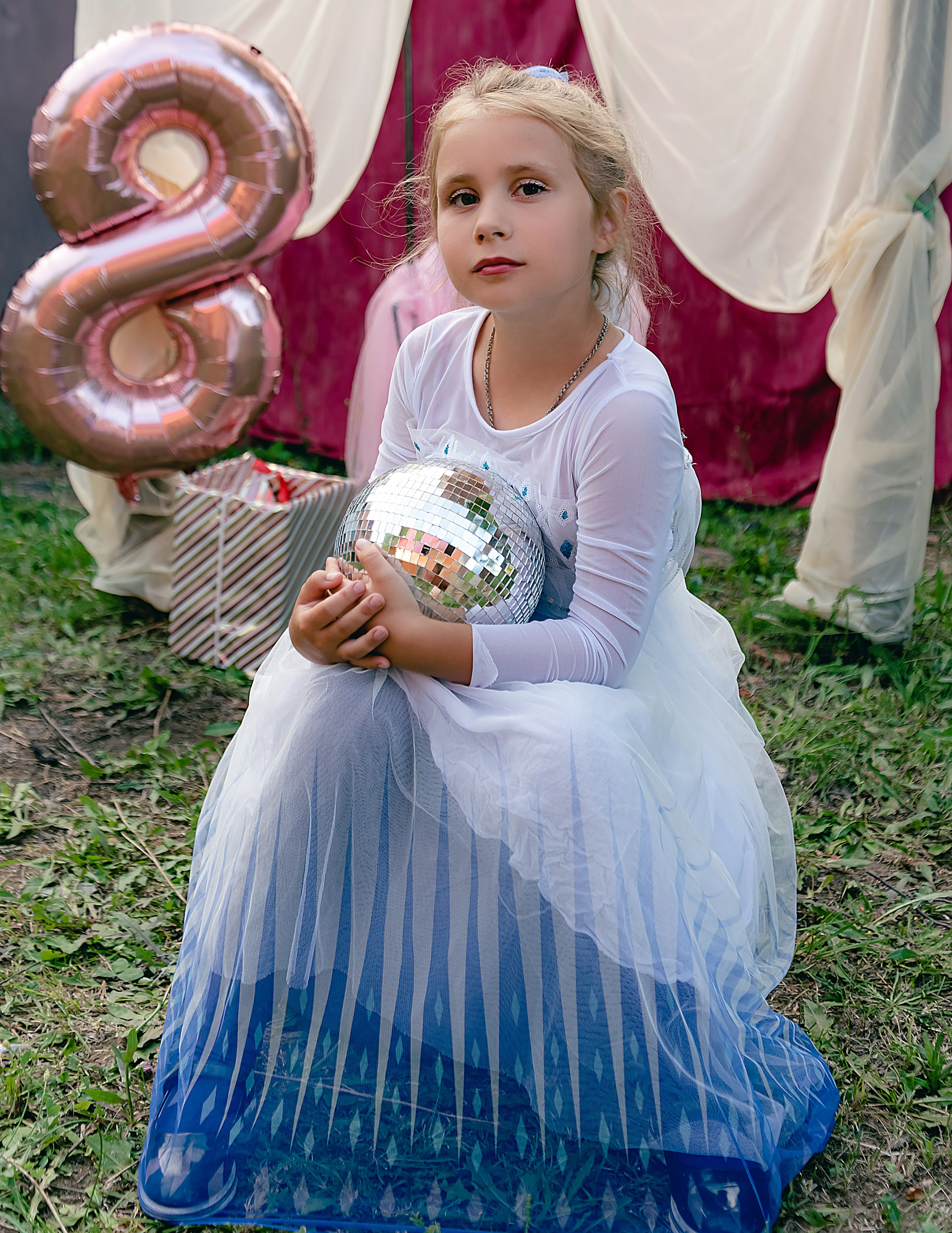 На фото девочка сидит с шариком около качелей.