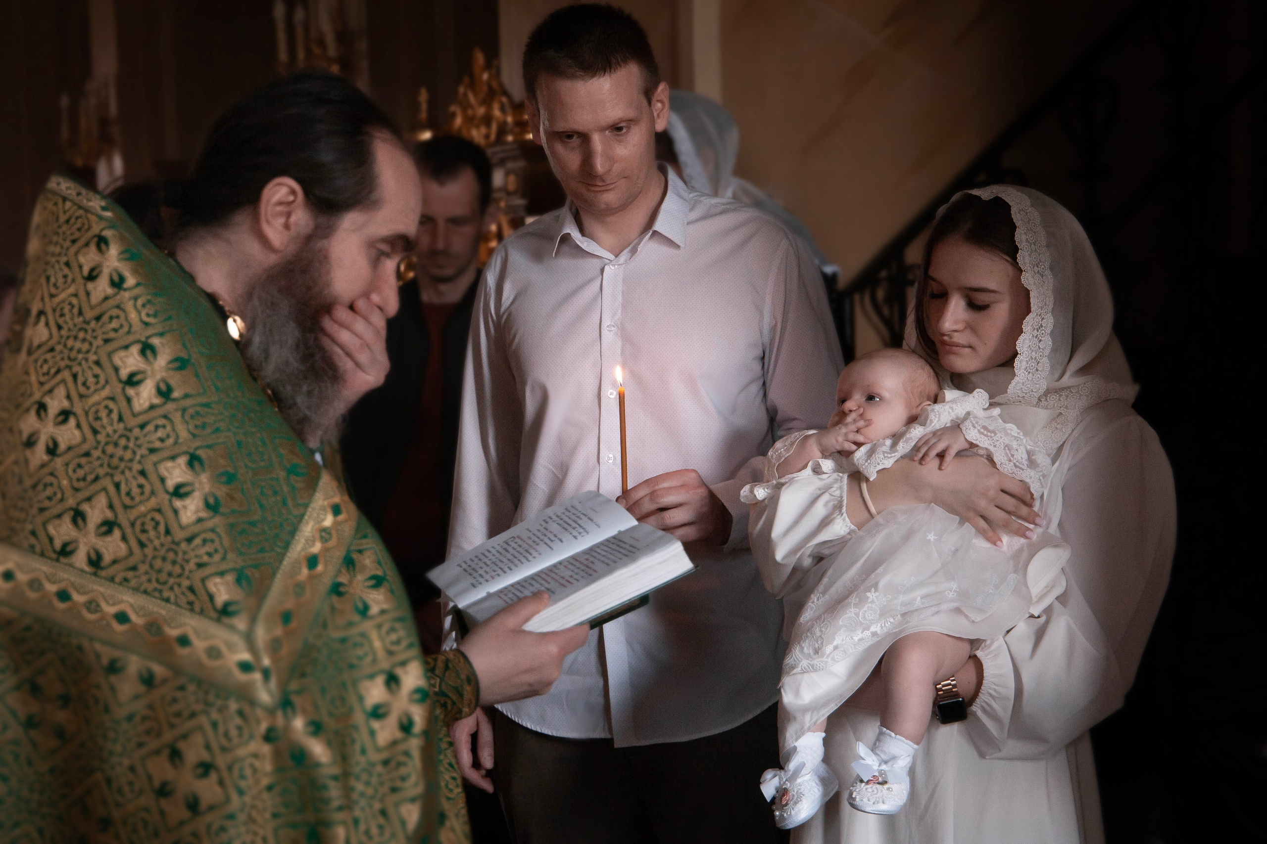 малышка на руках у крёстной мамы во время таинства крещения