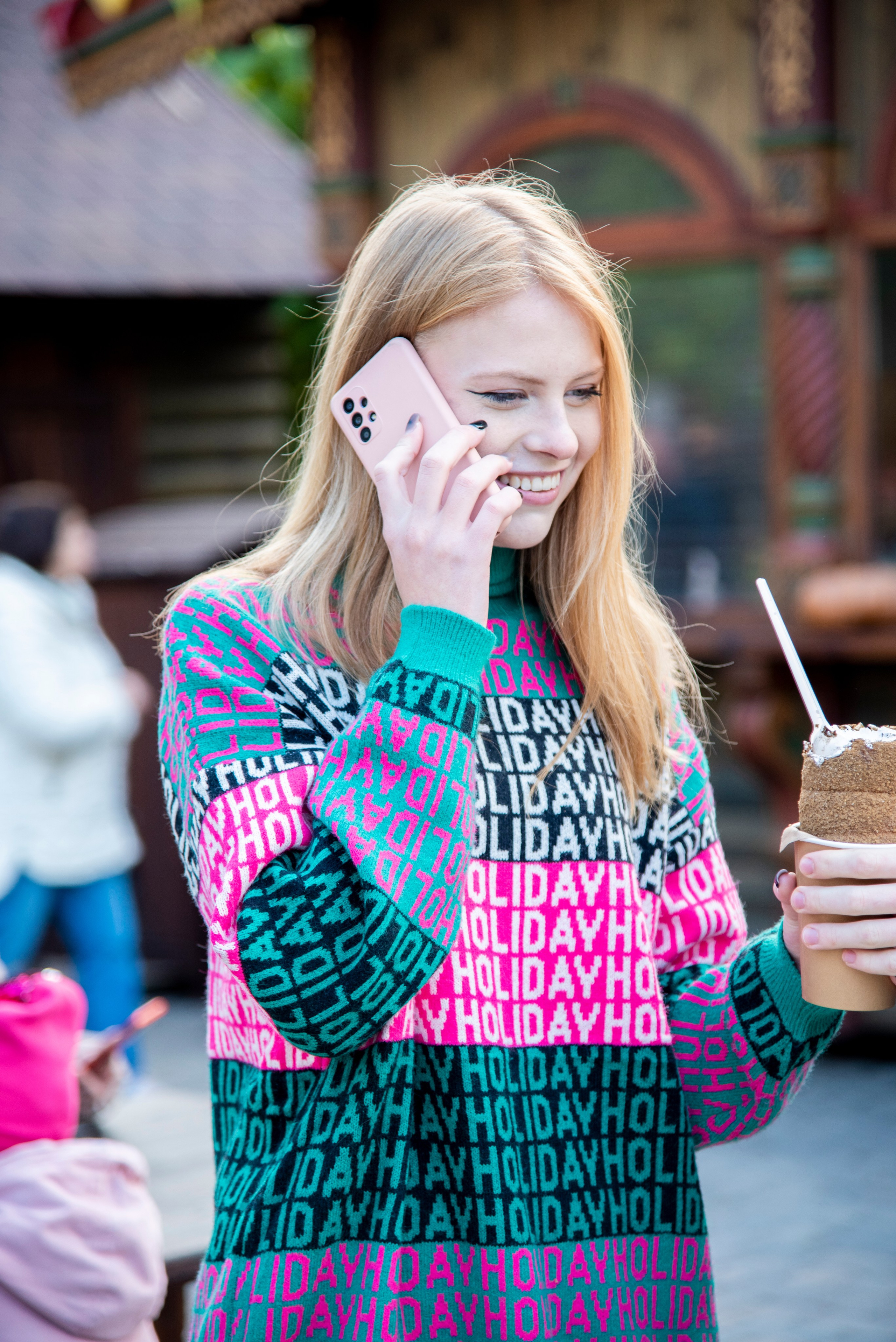 молодая девушка студентка. блондинка. длинные волосы. розово-зелёный свитер. парк Лога . осень с телефоном