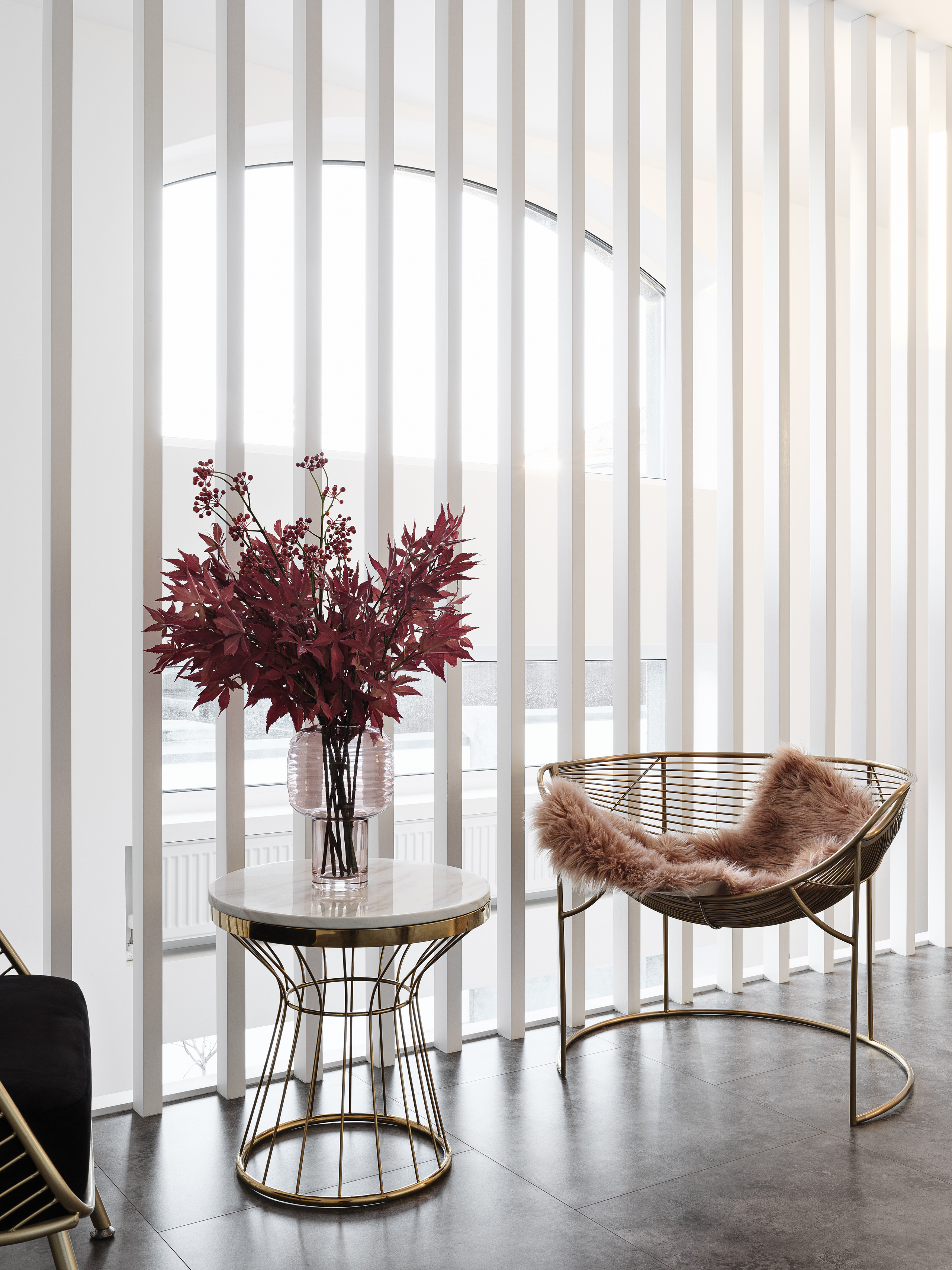 Ракурс на зону отдыха у окна: металлическое кресло с подушкой из искусственного меха, круглый столик с мраморной столешницей и букет в стеклянной вазе, белые рейки и панорамное окно. Интерьер от Ирины Вольхиной, стилист Марина Чернышева, фото Сергей Денисенко