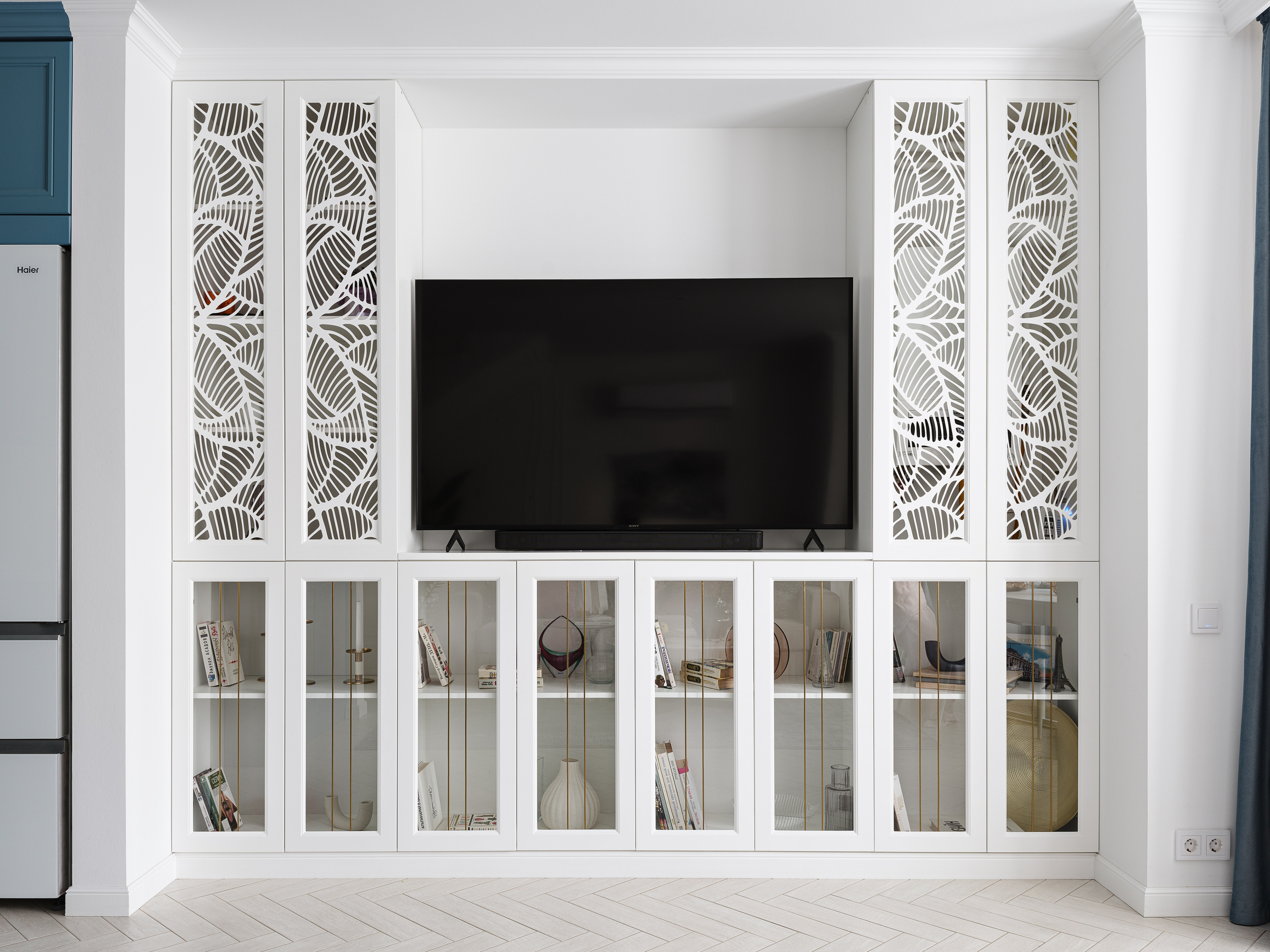 Белая ТВ-зона с декоративными панелями и витринами с книгами, современный дизайн интерьера гостиной от Светланы Олефиренко и Марии Морозовой, фотограф Сергей Денисенко, сочетание функциональности и элегантного стиля.